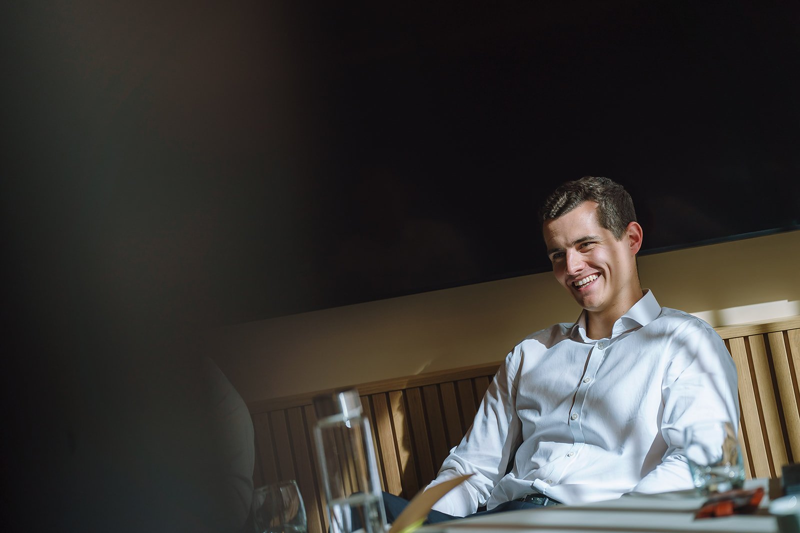Smiling man in a white button-down shirt seated at a restaurant table.
