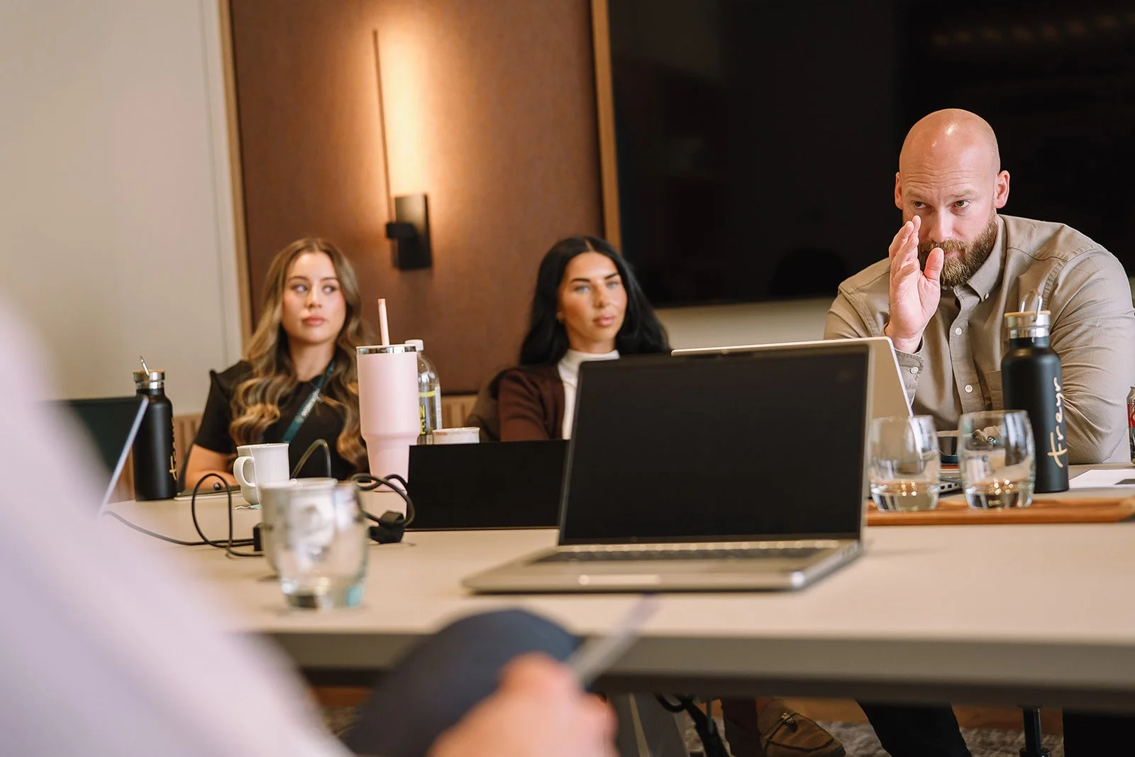 Business meeting with three colleagues seated at a conference table, laptop and drinks in foreground