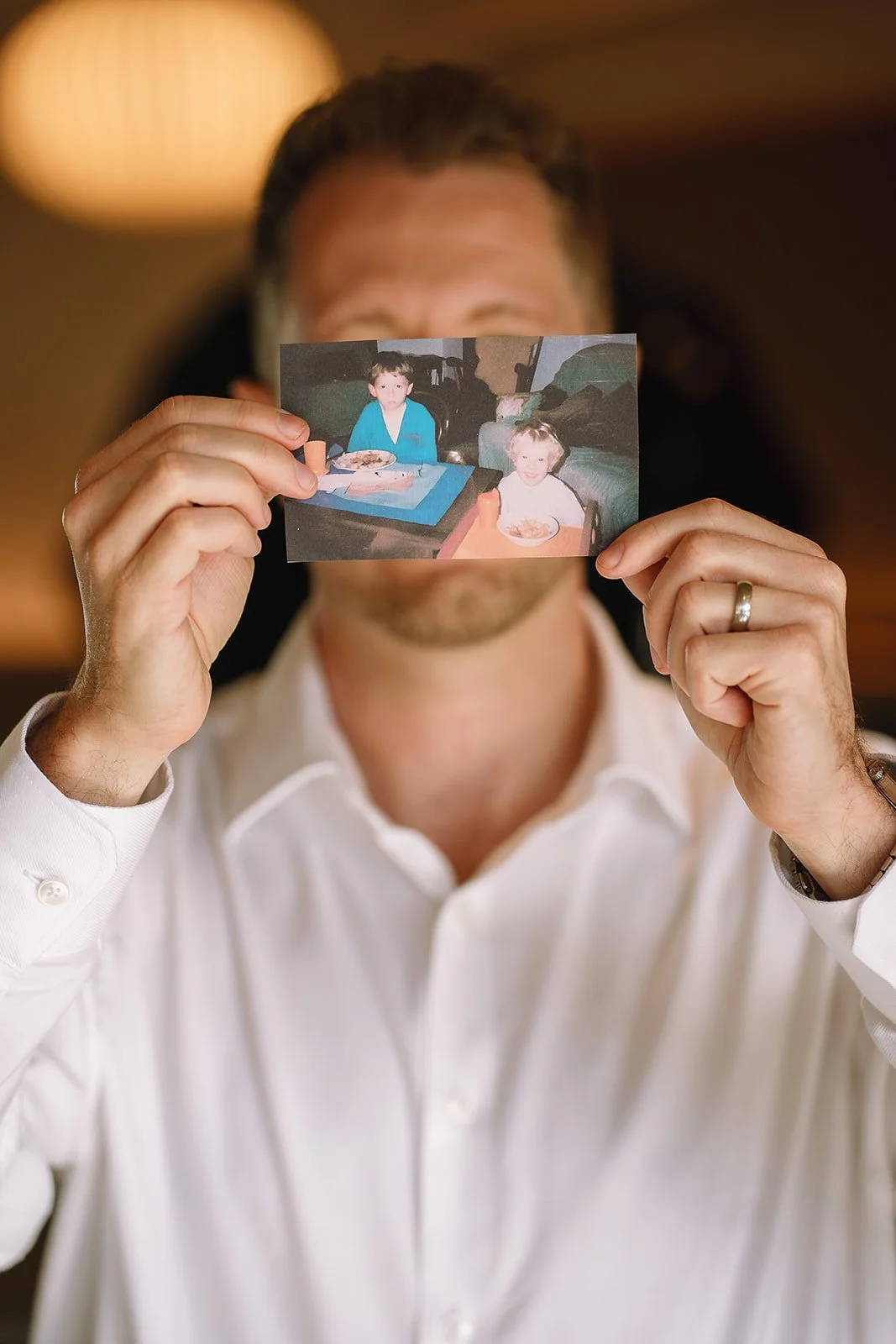 Man in a white shirt holding a childhood photo of two children eating at a table