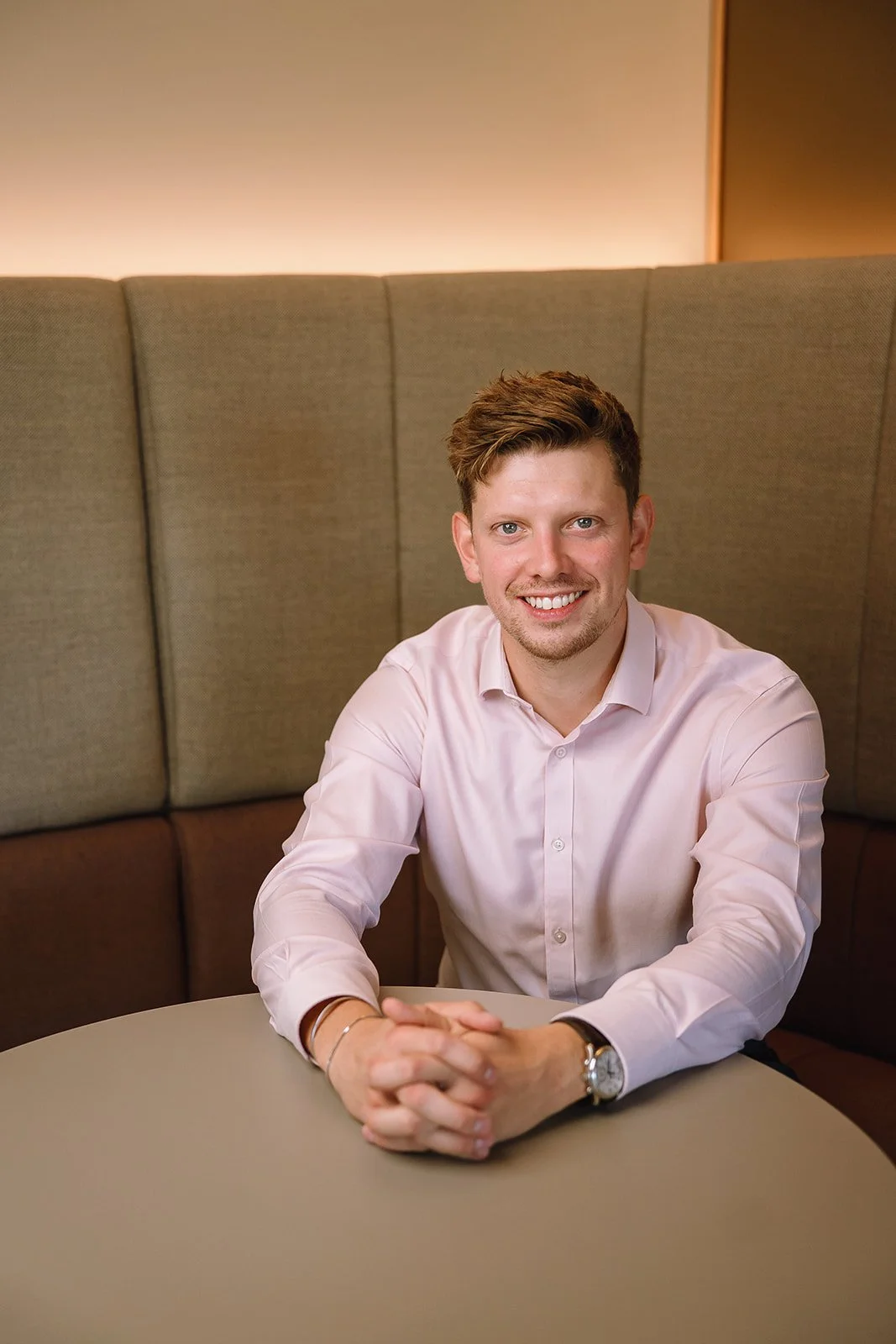 Smiling man in a pink button-down shirt seated at a restaurant table.