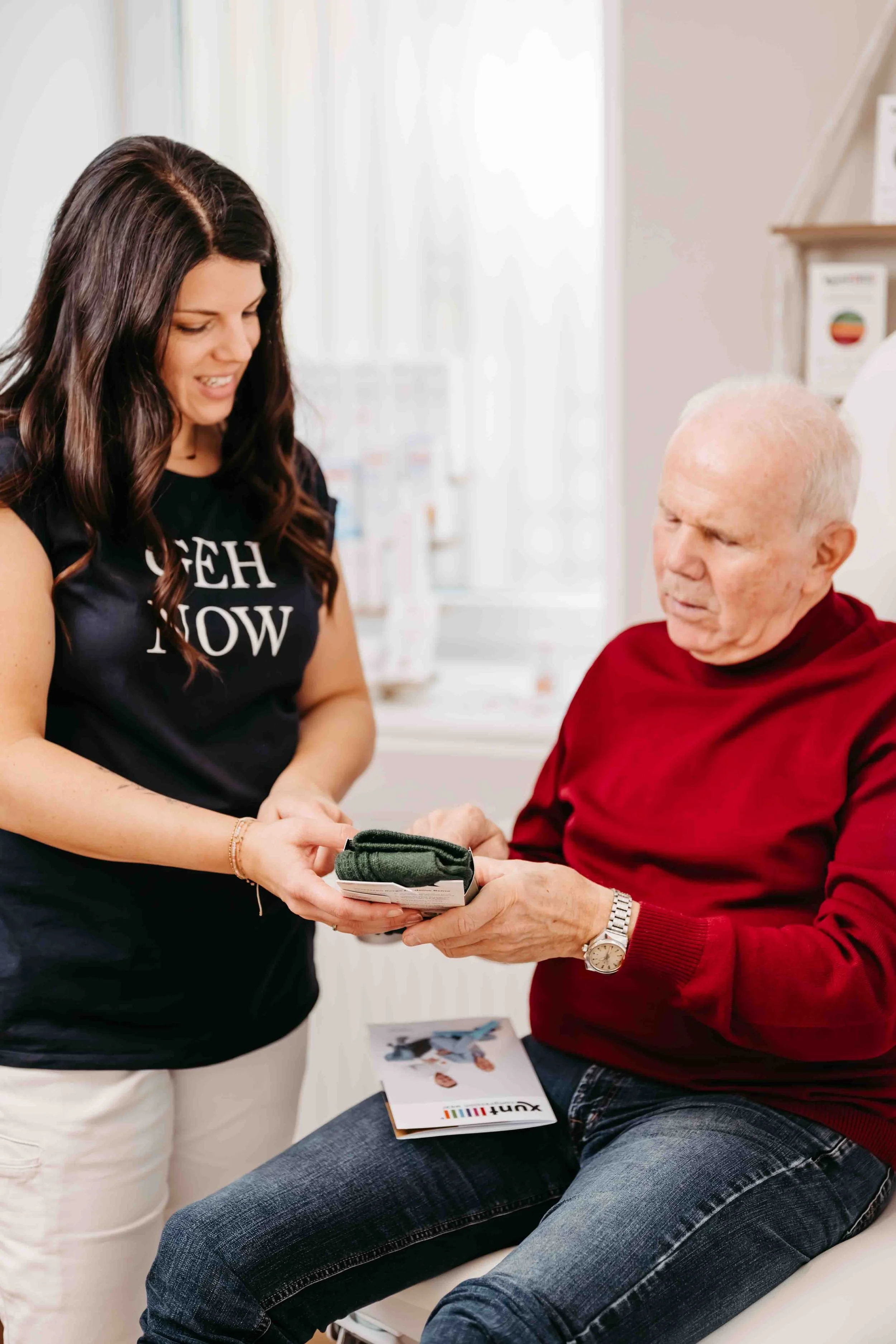 Junge Frau übergibt einem älteren Mann ein Paket in einer medizinischen Einrichtung.