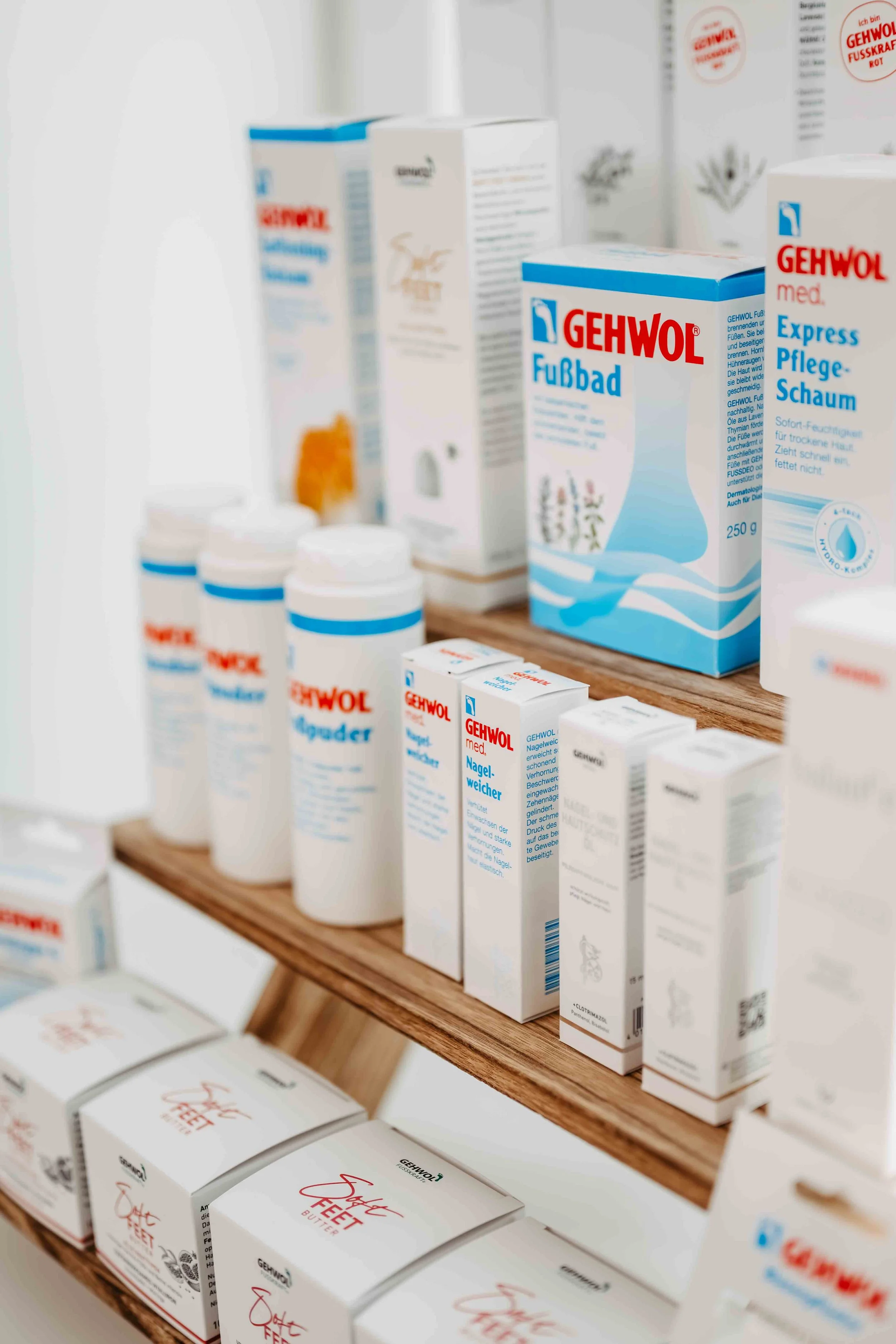 Verschiedene medizinische Produkte und Cremes von der Marke Gehwol auf einem Holzregal, darunter Fußbader, Nagelweicher und Pflegecremes.