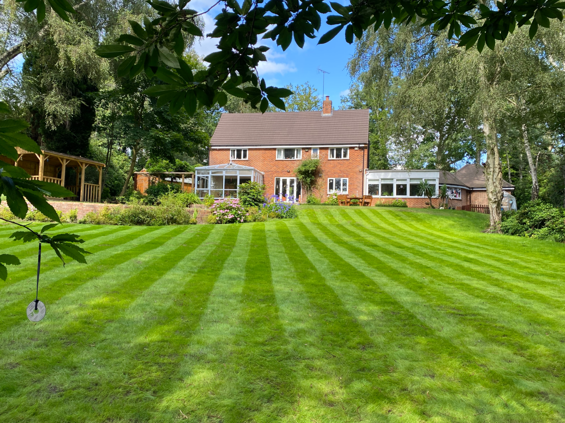 Mown lawn leading down to a house and planted garden