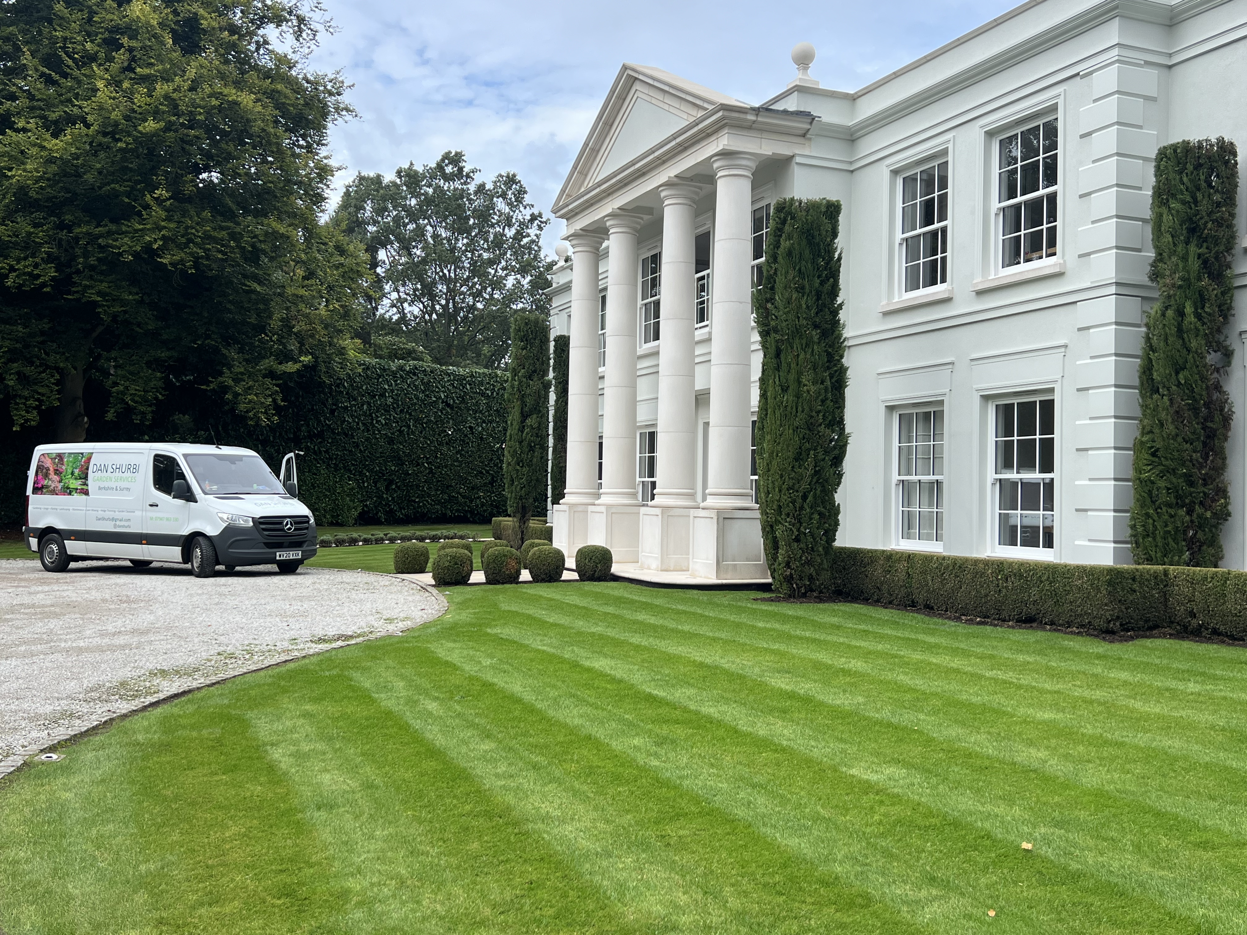 Freshly mown, striped lawn in front of a white house with columns and a Dan Shurbi branded van parked in front of the house