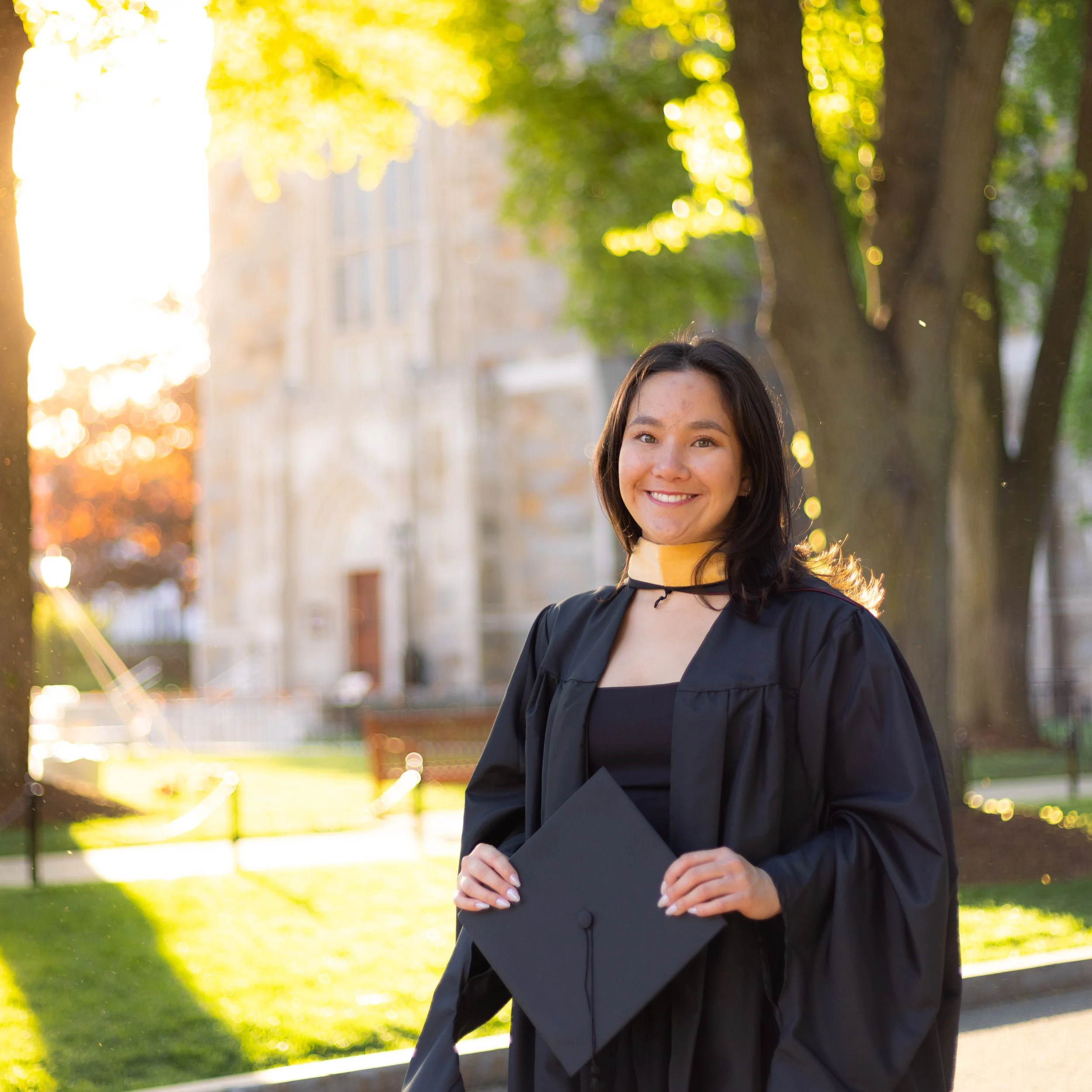 A graduate holding her cap in front of a beautiful chapel on campus