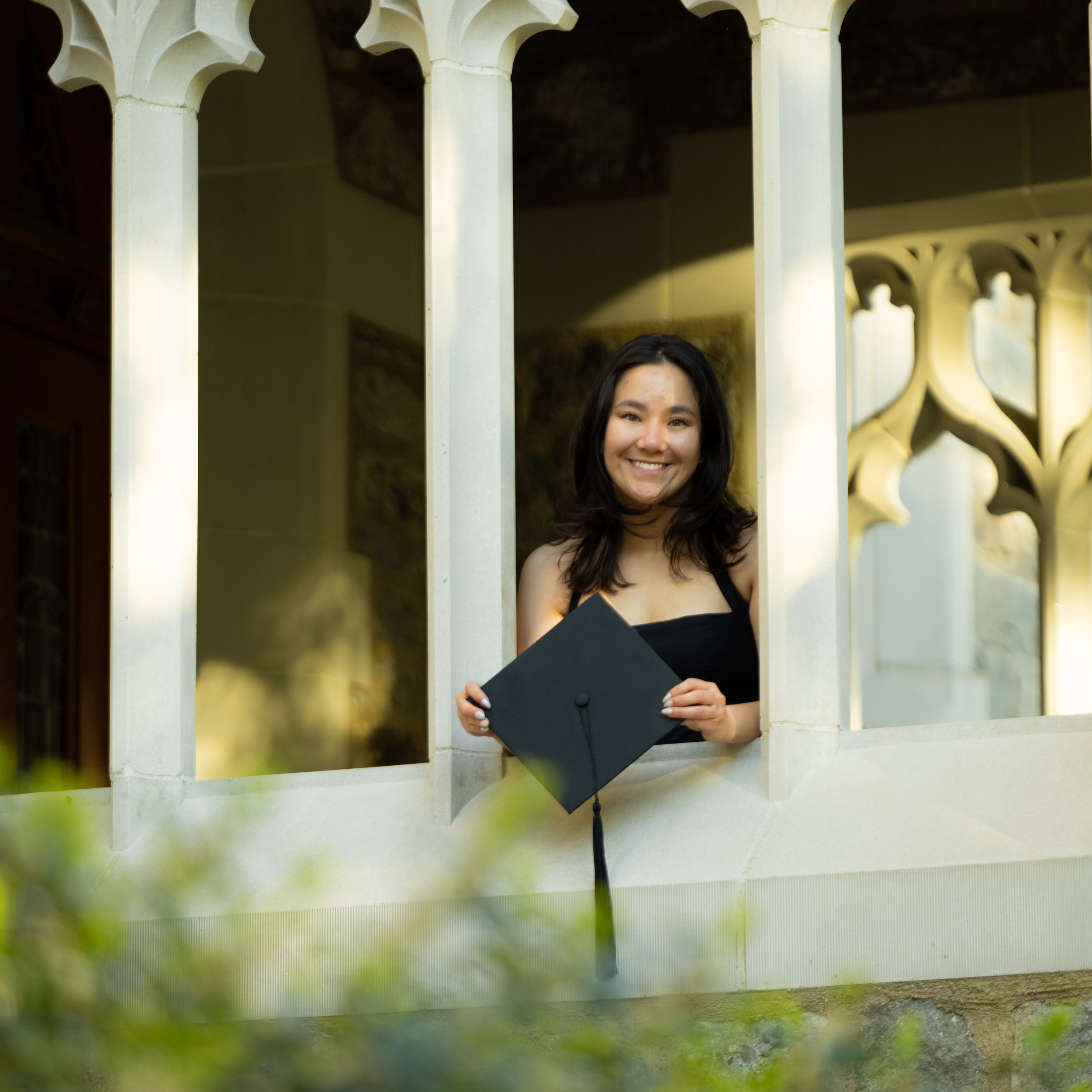 A graduate peeking head out of an opening in a building to show their graduation cap