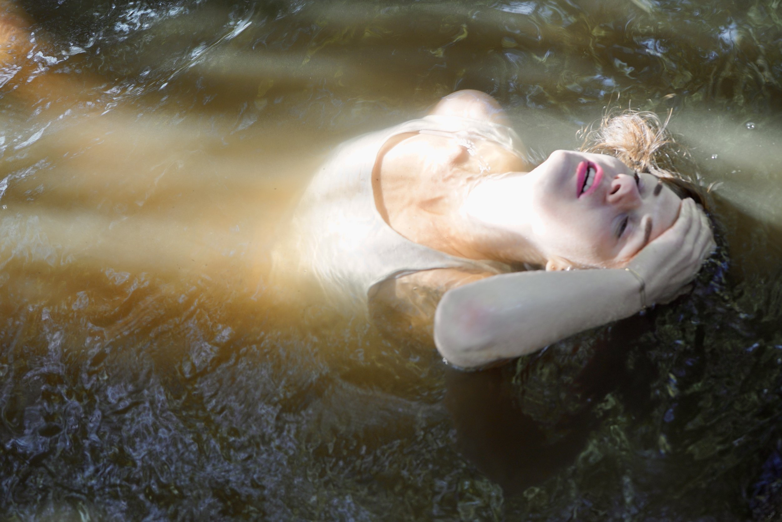 A woman floating in a body of water with her eyes closed and one hand on her head.