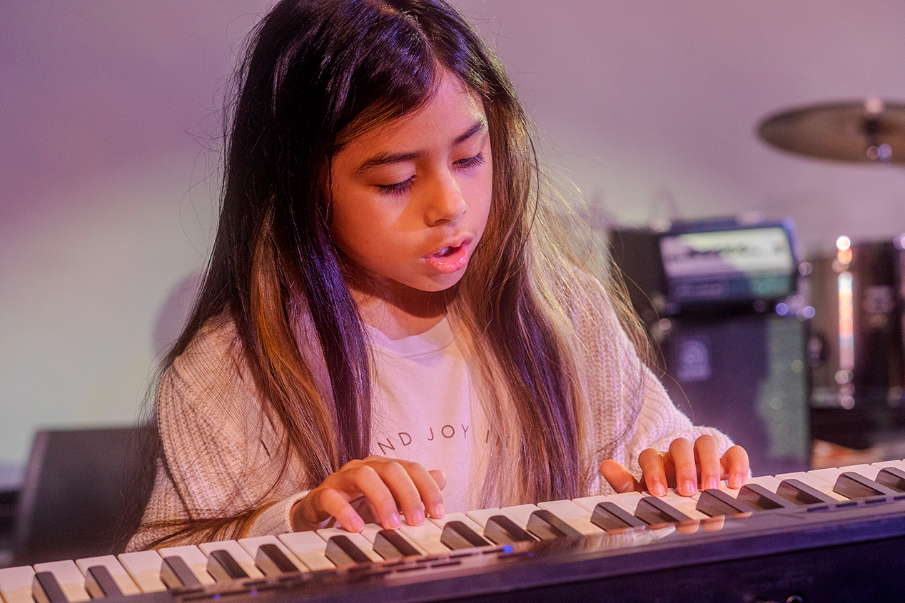 A young girl playing a keyboard piano with a focused expression