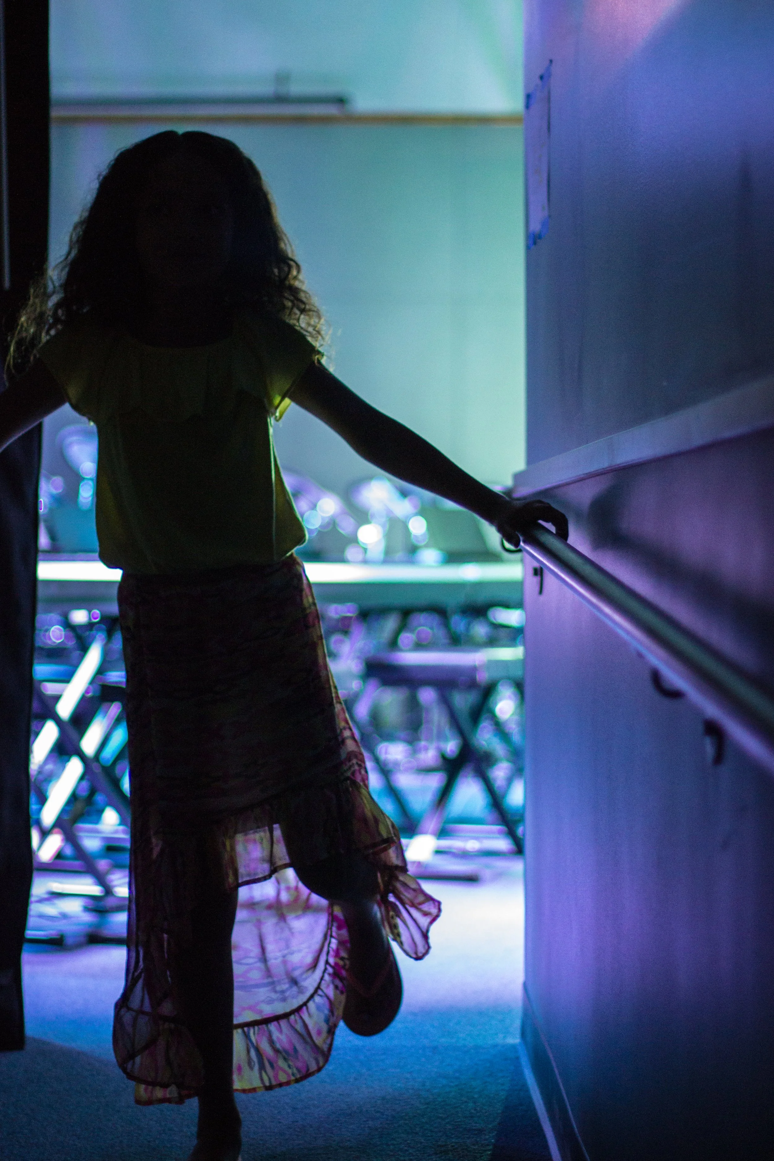 Silhouette of a girl in a colorful dress walking down a hallway with blue and purple lighting.