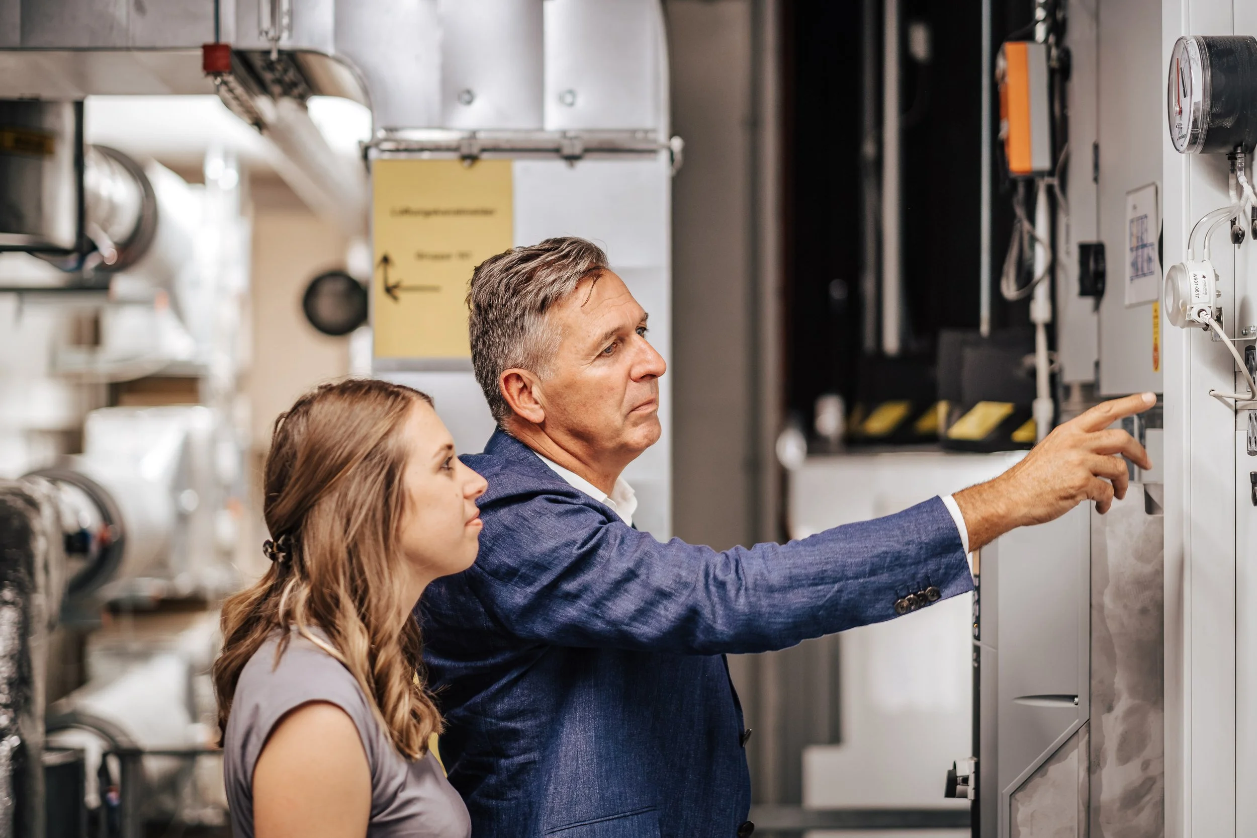 Zwei Menschen, ein Mann und eine Frau, schauen auf ein technisches Gerät in einem technischen Raum.