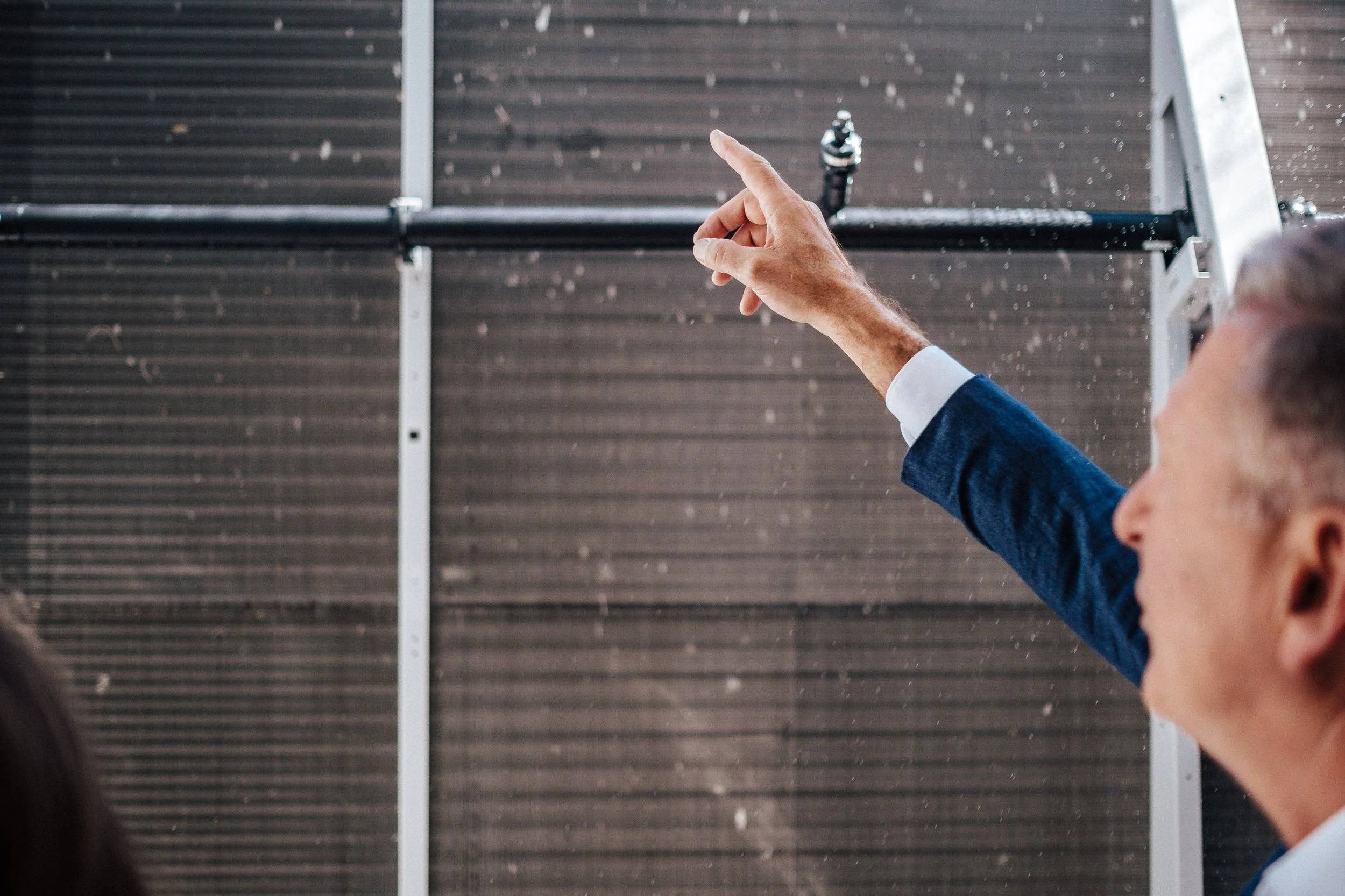 Ein Mann in Anzug zeigt auf eine Solaranlage im Hintergrund.