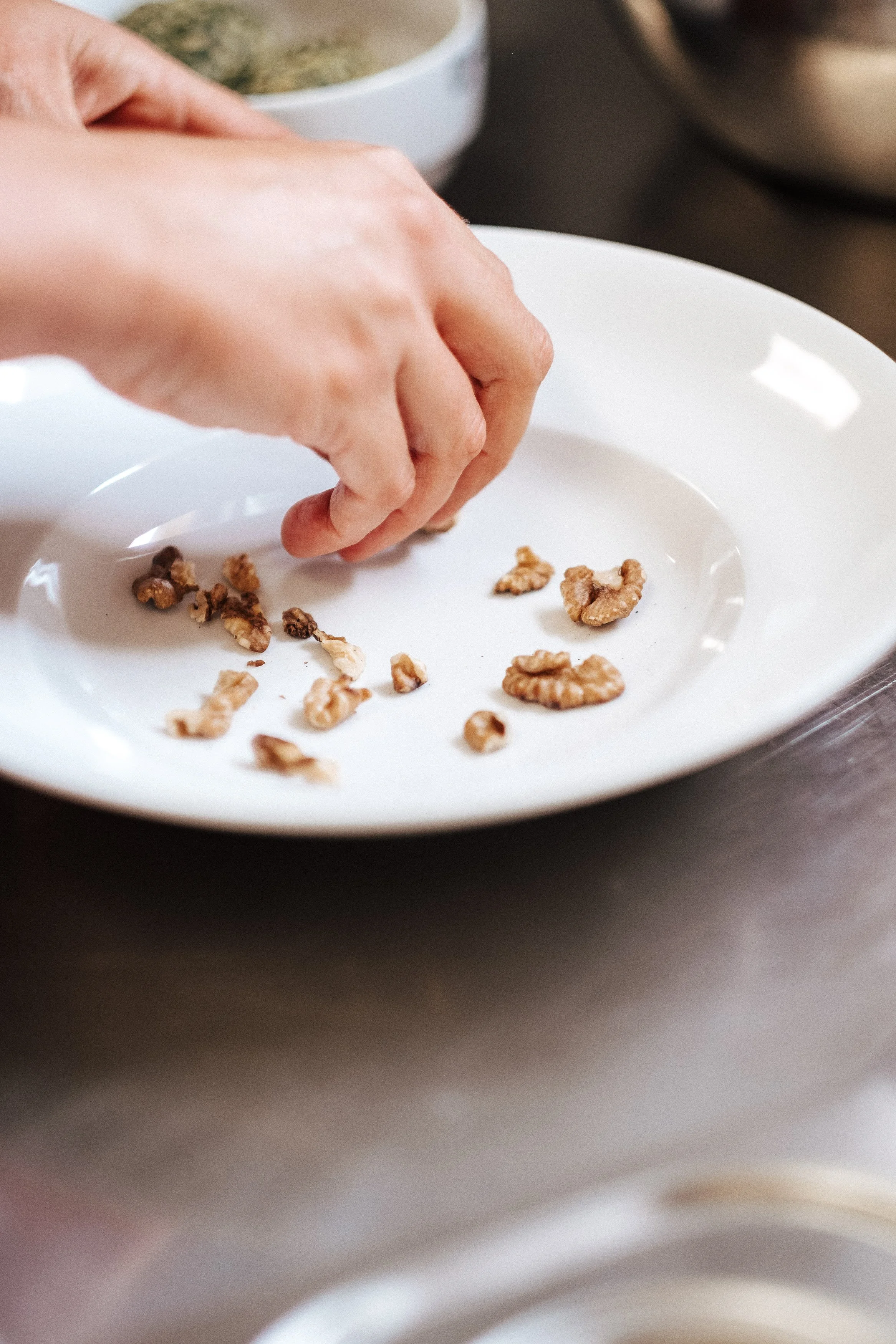 Person streut Walnüsse auf einen weißen Teller