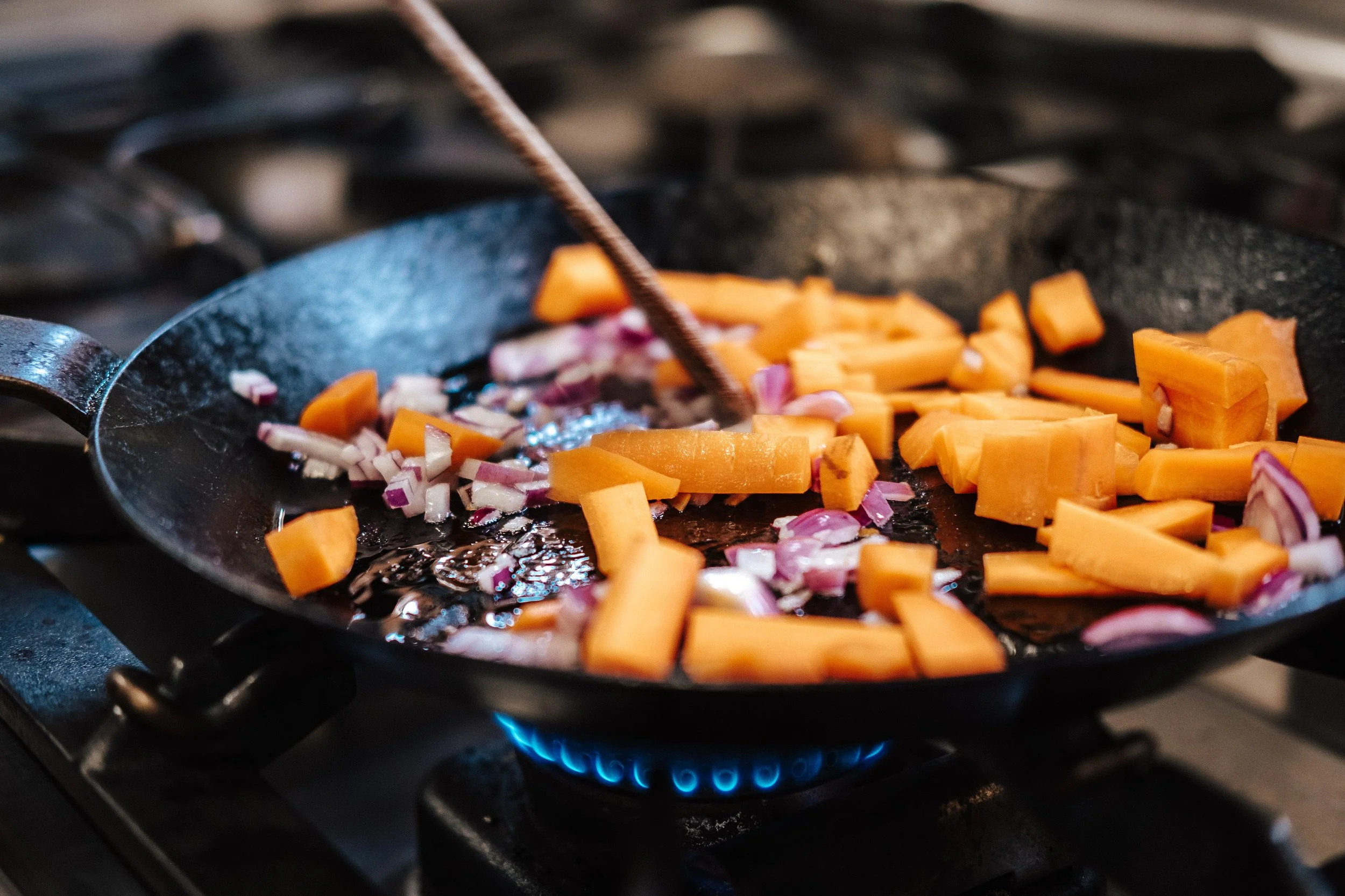Karotten und Zwiebeln werden in einer Pfanne auf einem Herd angebraten.