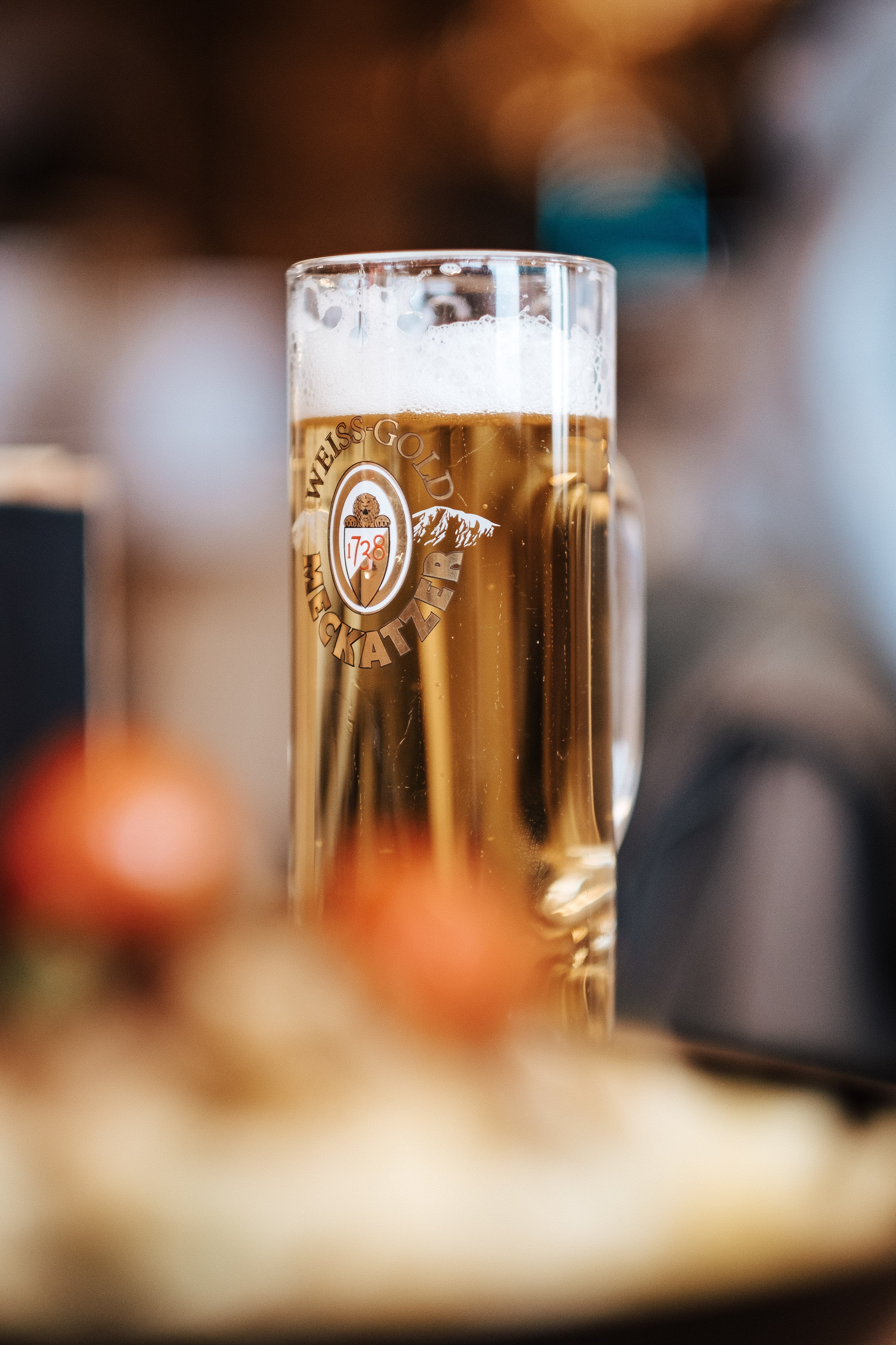 Ein Glas Bier in einem Bierglas mit einem Logo, das einen Berg, einen Rehkadaver und die Schrift 'Weiss-Gold Brauerei' zeigt, steht auf einem Tisch.