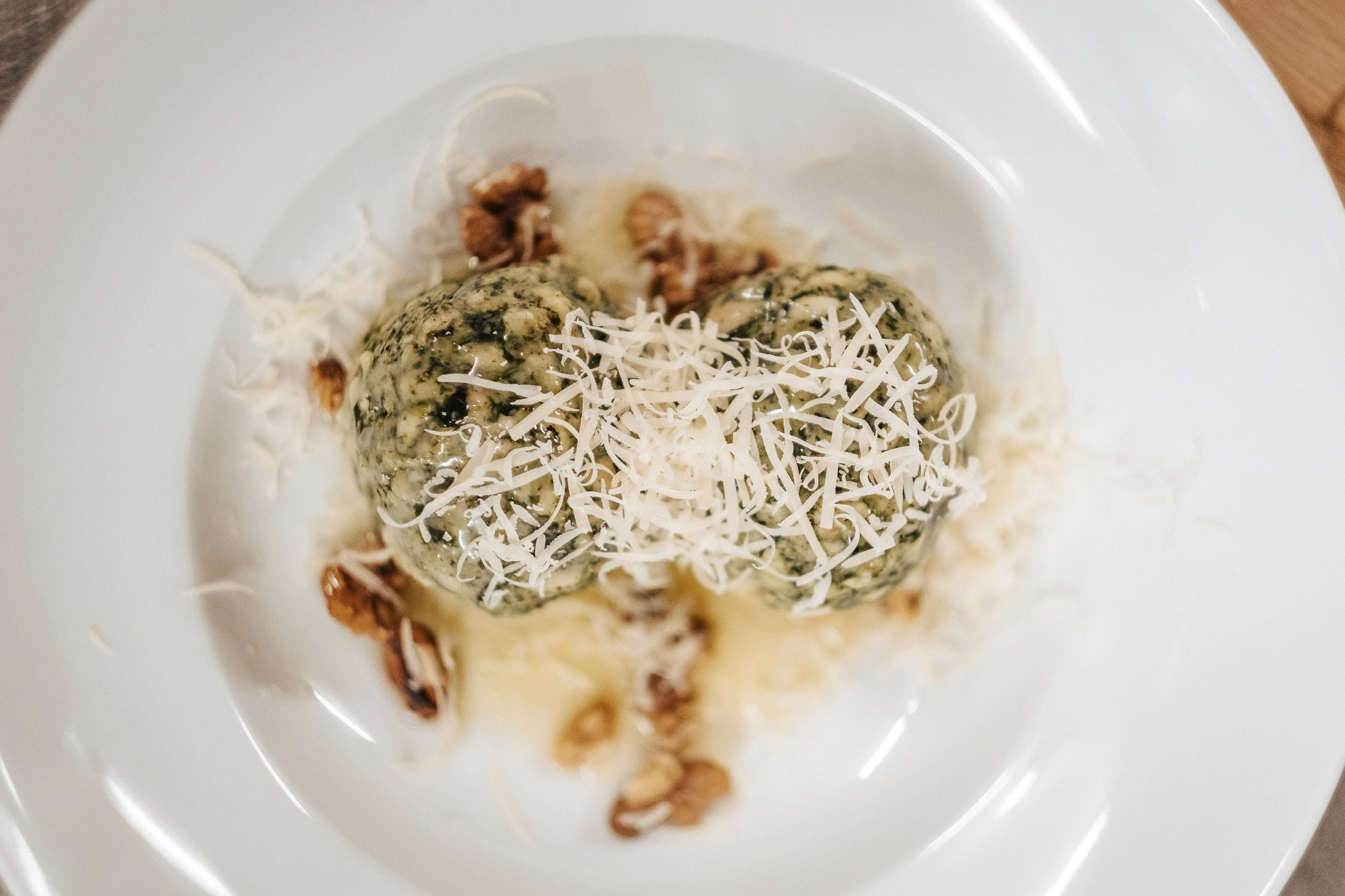 Bällchen aus Spinat und Käse, mit geriebenem Käse und Walnüssen serviert auf einem weißen Teller.