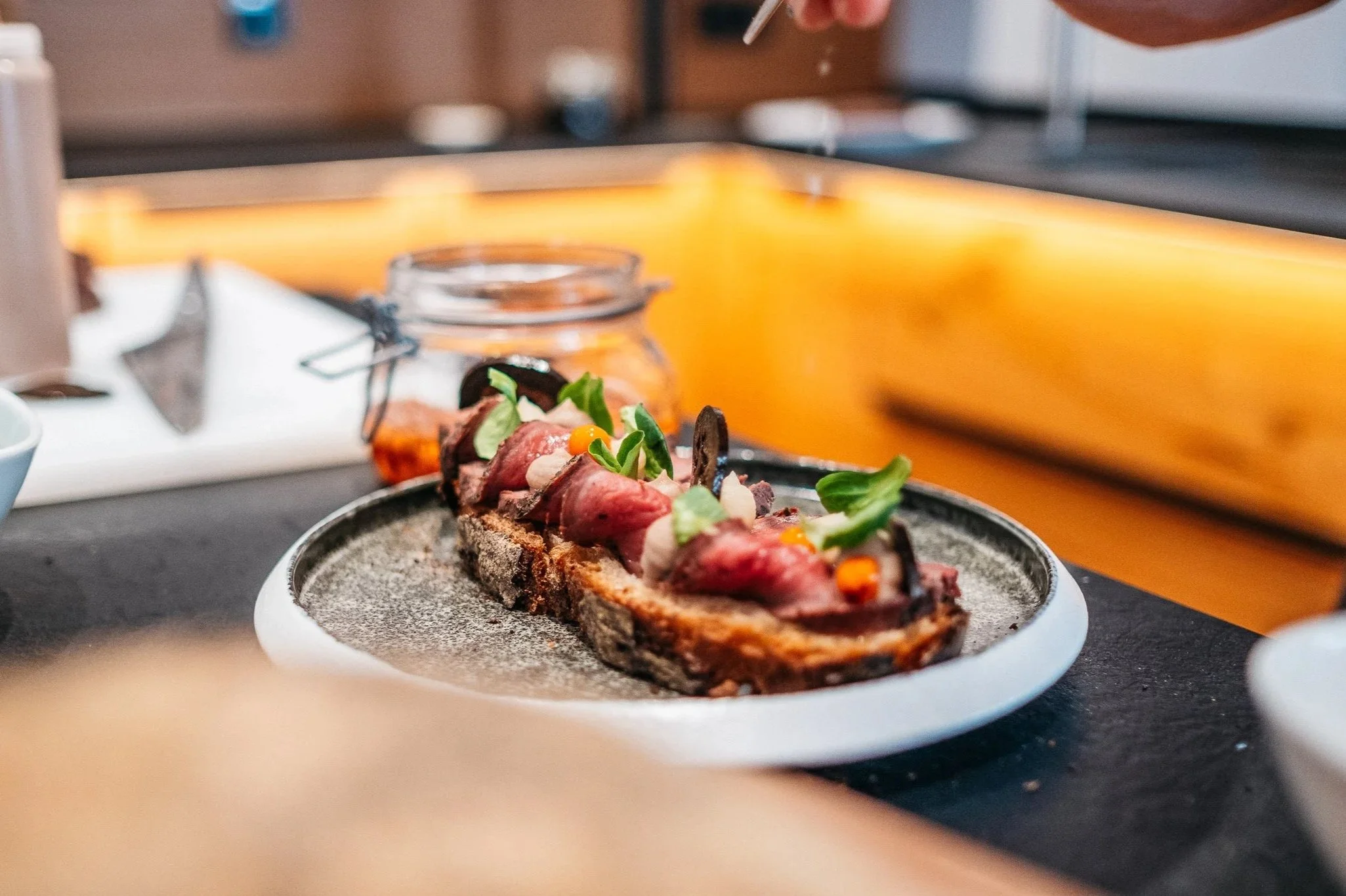 Brot mit rohem Rindfleisch, Kräutern und kleineren Beilagen auf einem schwarzen Teller