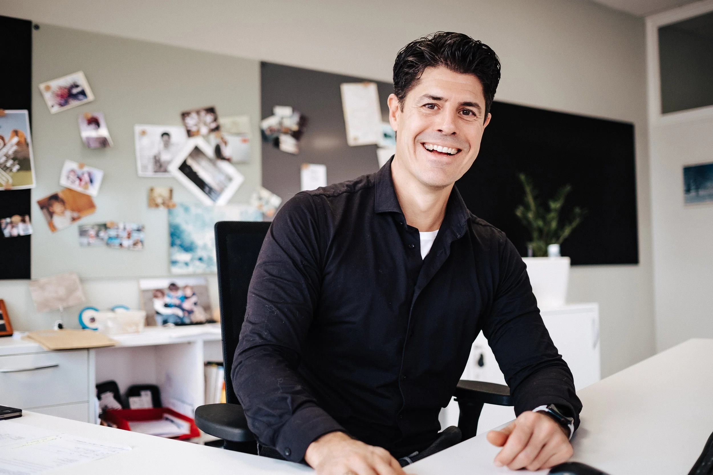 Lächelnder Mann in einem modernen Büro, sitzend an einem weißen Tisch.