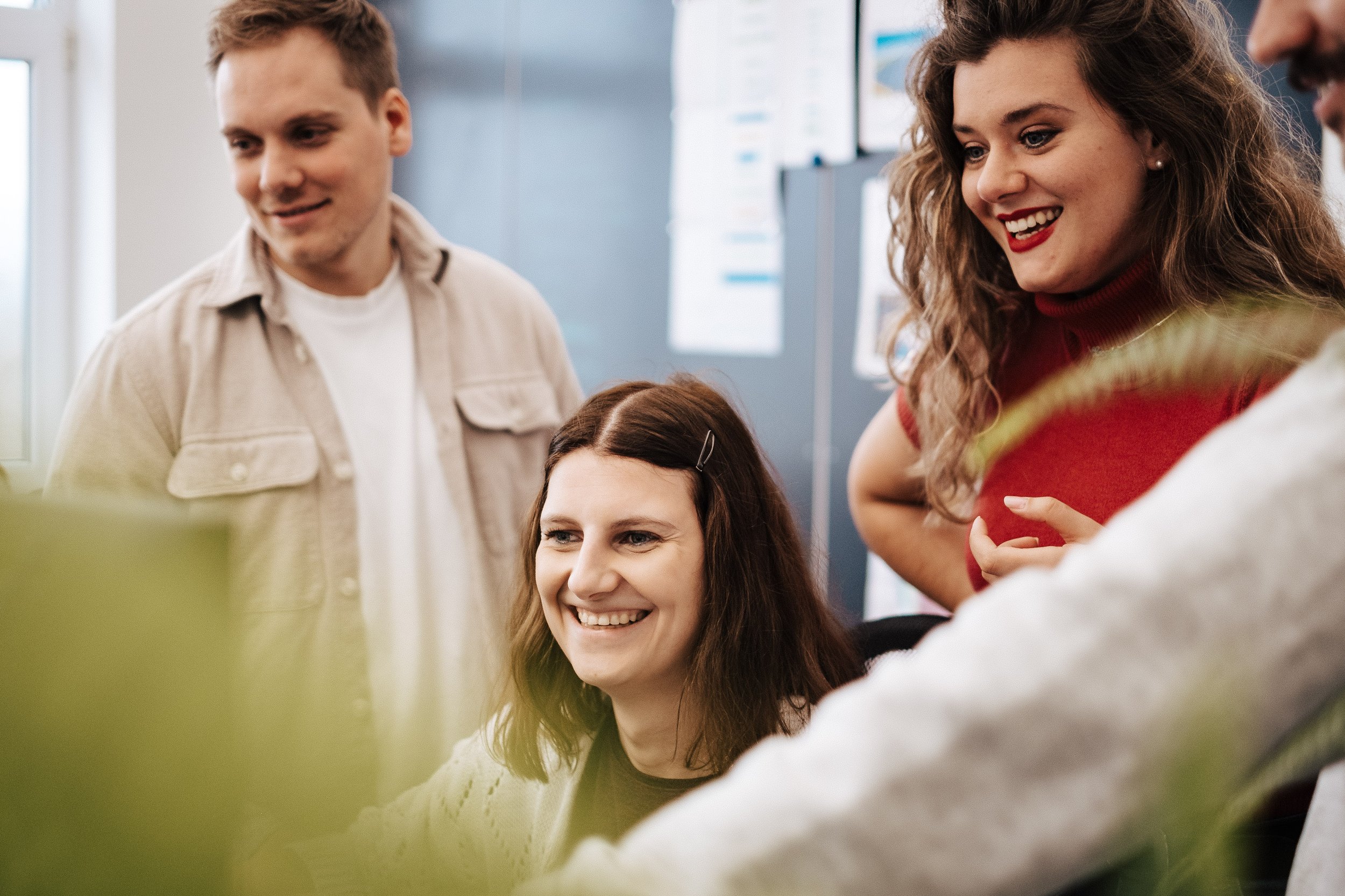 Gruppe junger Menschen arbeitet zusammen an einem Projekt in einem Büro, lächelt und diskutiert.