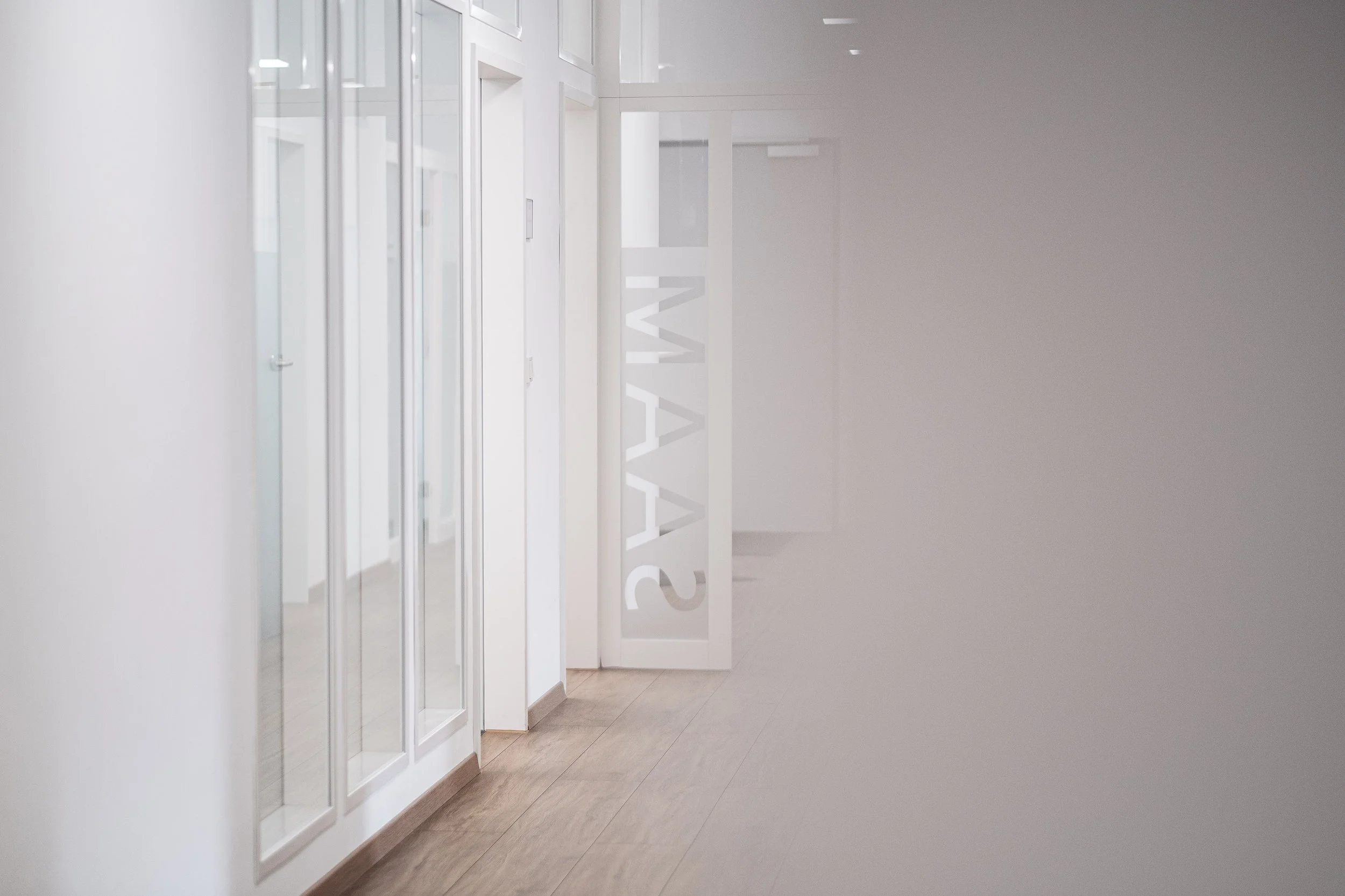 Ein weißer Flur mit Glastüren und einem Sichtschutz mit dem Wort 'STAFF' auf einer Wand.