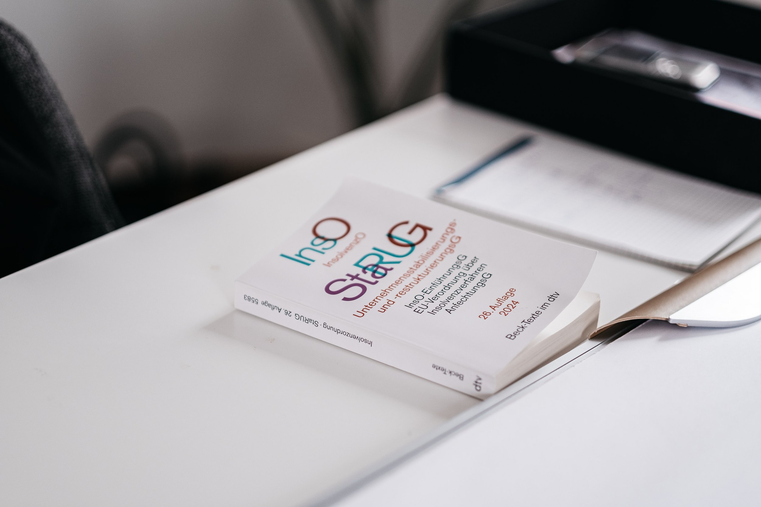 Ein Buch mit dem Titel 'Instandsetzung Fachinfo' liegt auf einem weißen Tisch, neben einer Schreibmappe und einem Notizbuch.