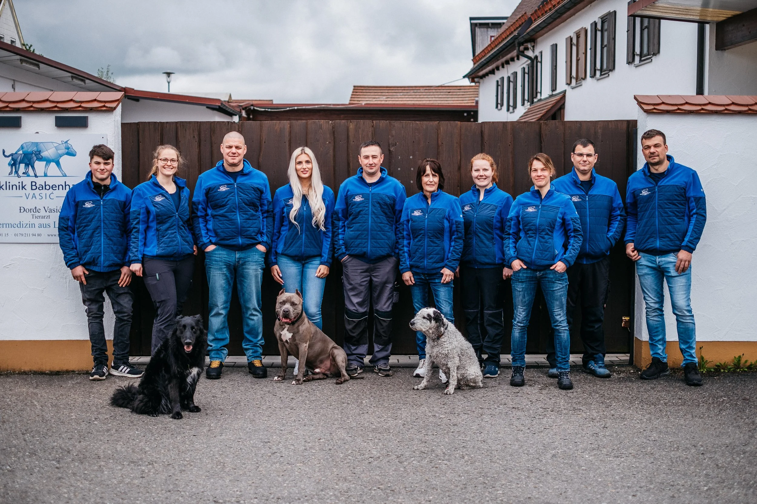Gruppenfoto eines Teams von Tierärzten vor der Tierklinik, alle in blauen Jacken, mit vier Hunden sichtbares, in einer Einfahrt vor einer Tierklinikkaus der Tierklinik Babenhausen.