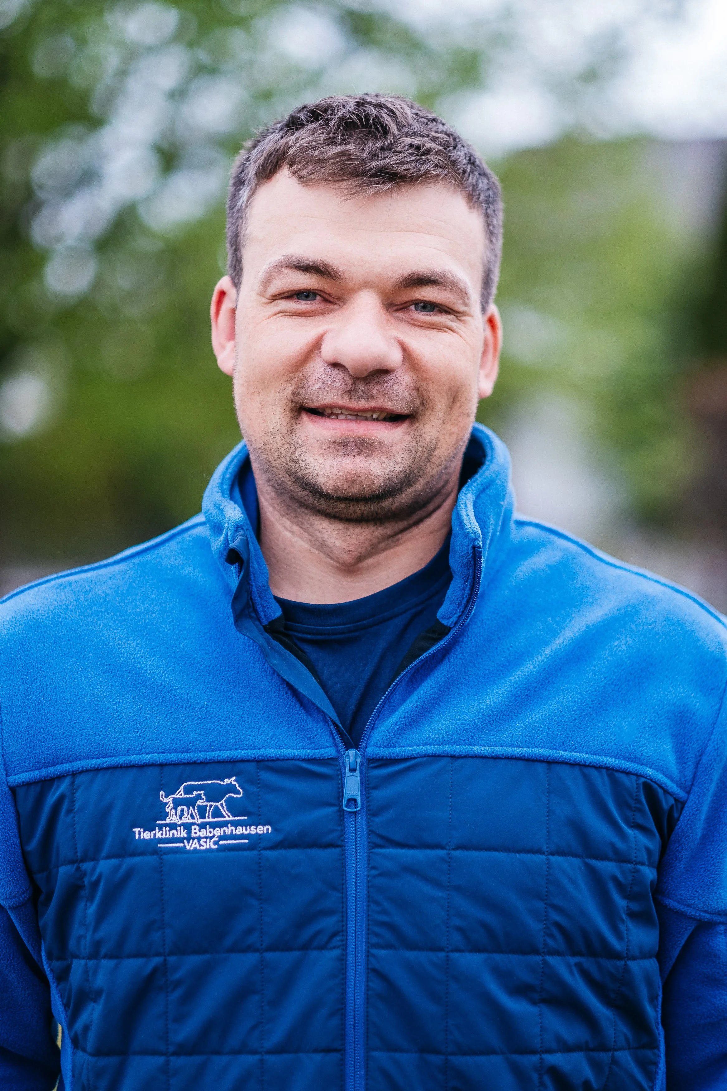 Mann in blauer Jacke mit Logo der Tierklinik Babenhausen, lächelnd im Freien