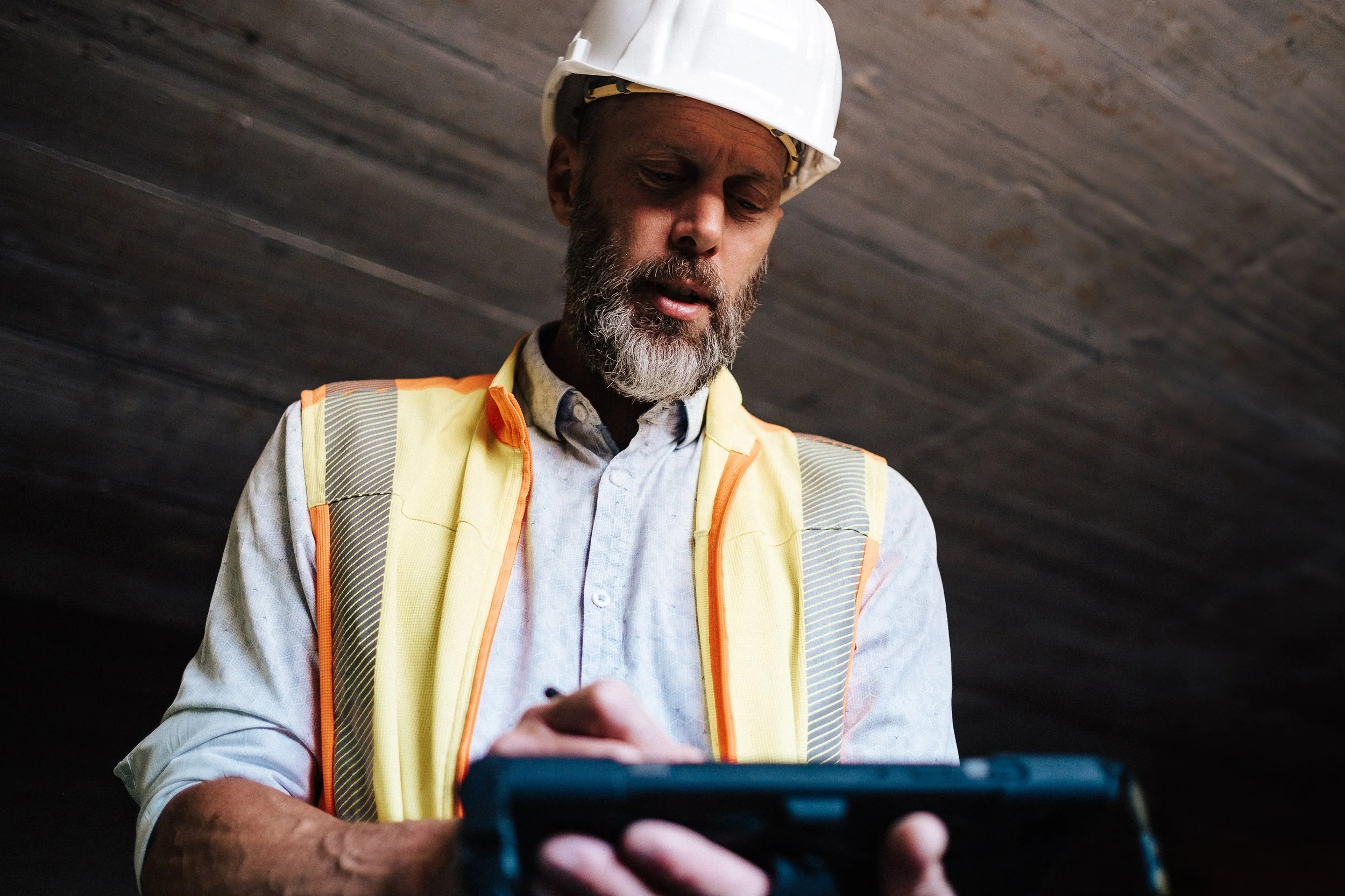 Ein Bauarbeiter mit weißem Helm und gelber Sicherheitsweste, der auf einem Tablet schaut.