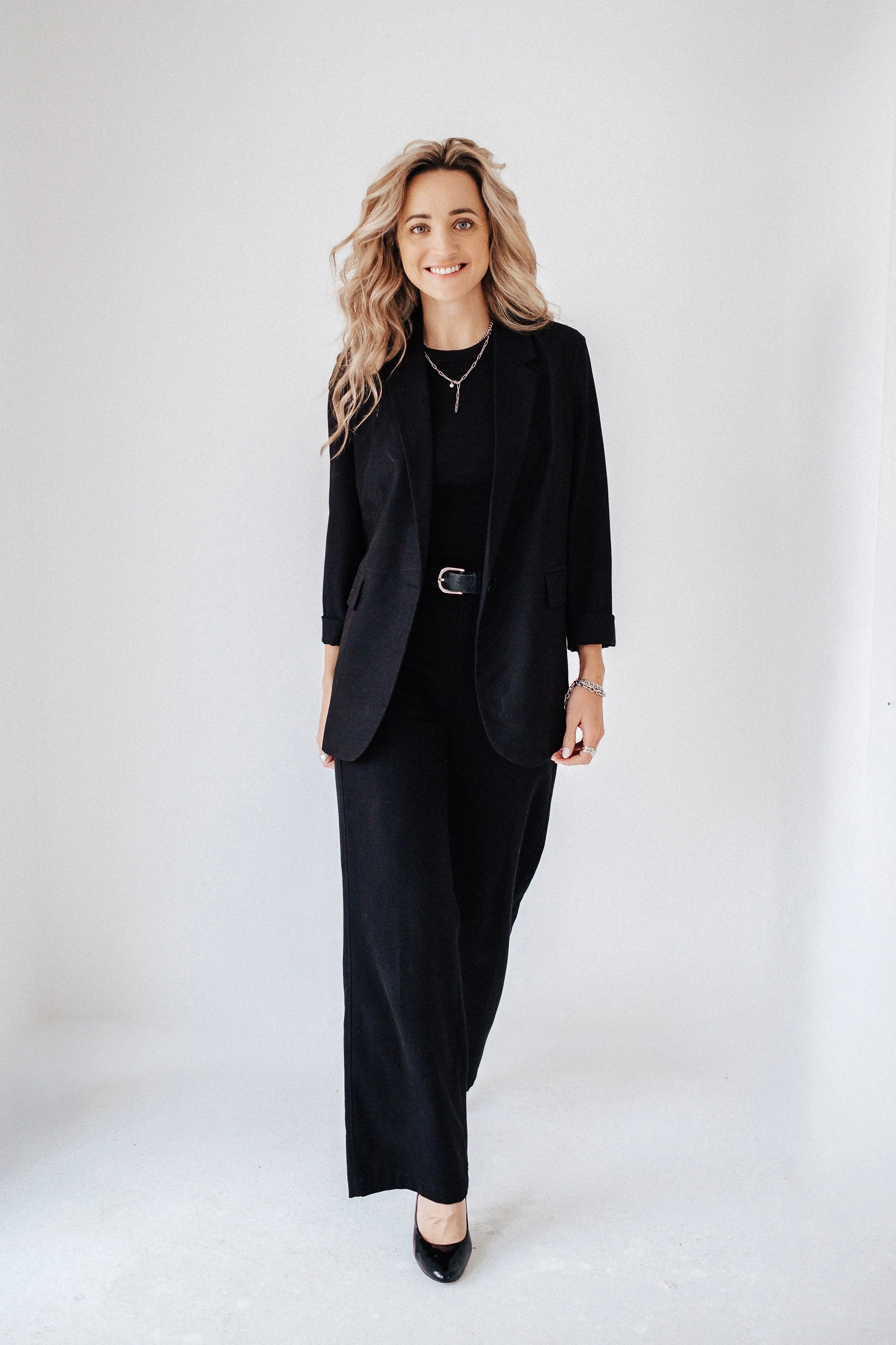 Eine elegante Frau in einem schwarzen Anzug, die in einen leeren Raum geht und lächelt.