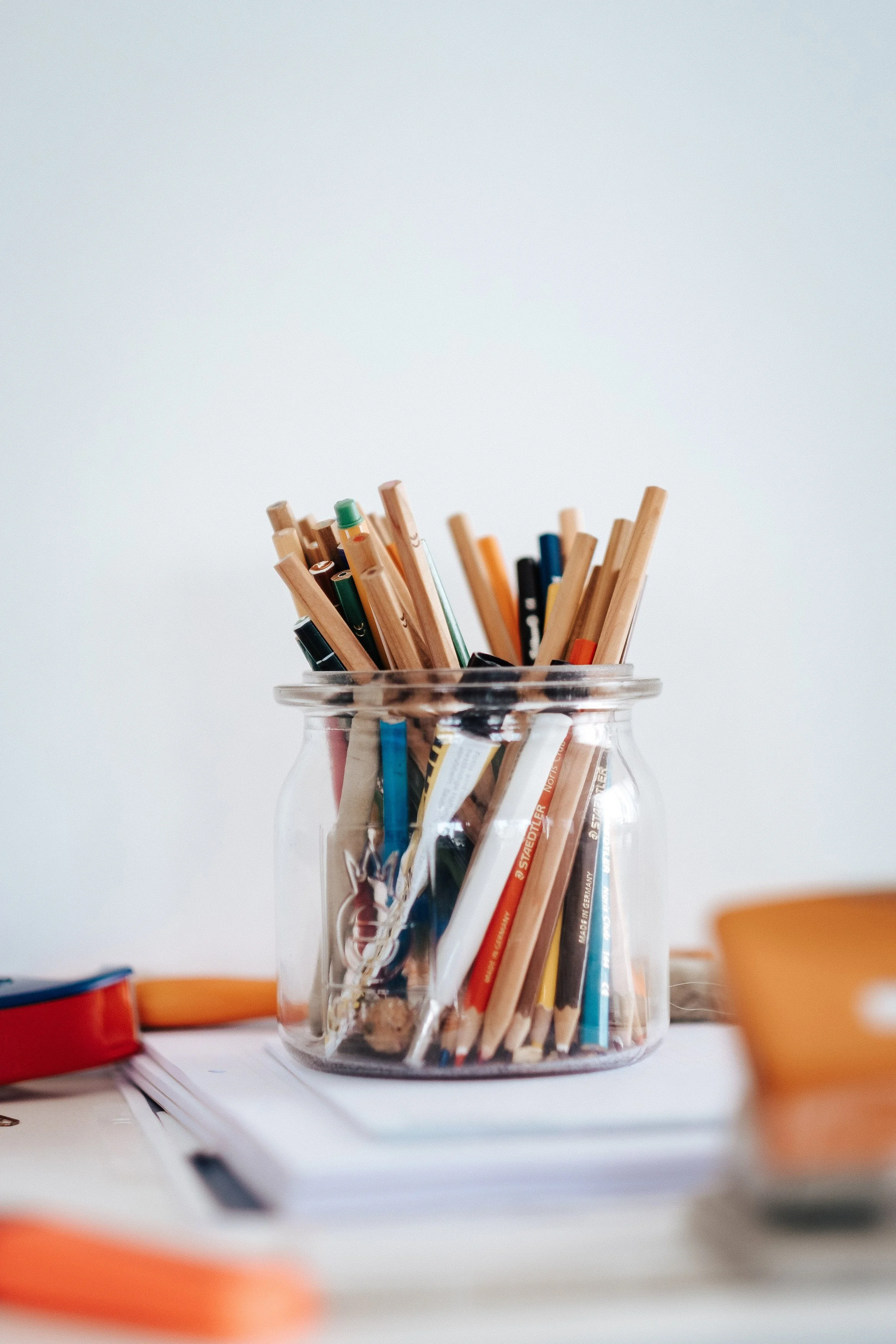 Ein Glaskrug mit Stiften und Bleistiften auf einem Schreibtisch, umgeben von anderen Schreibutensilien.