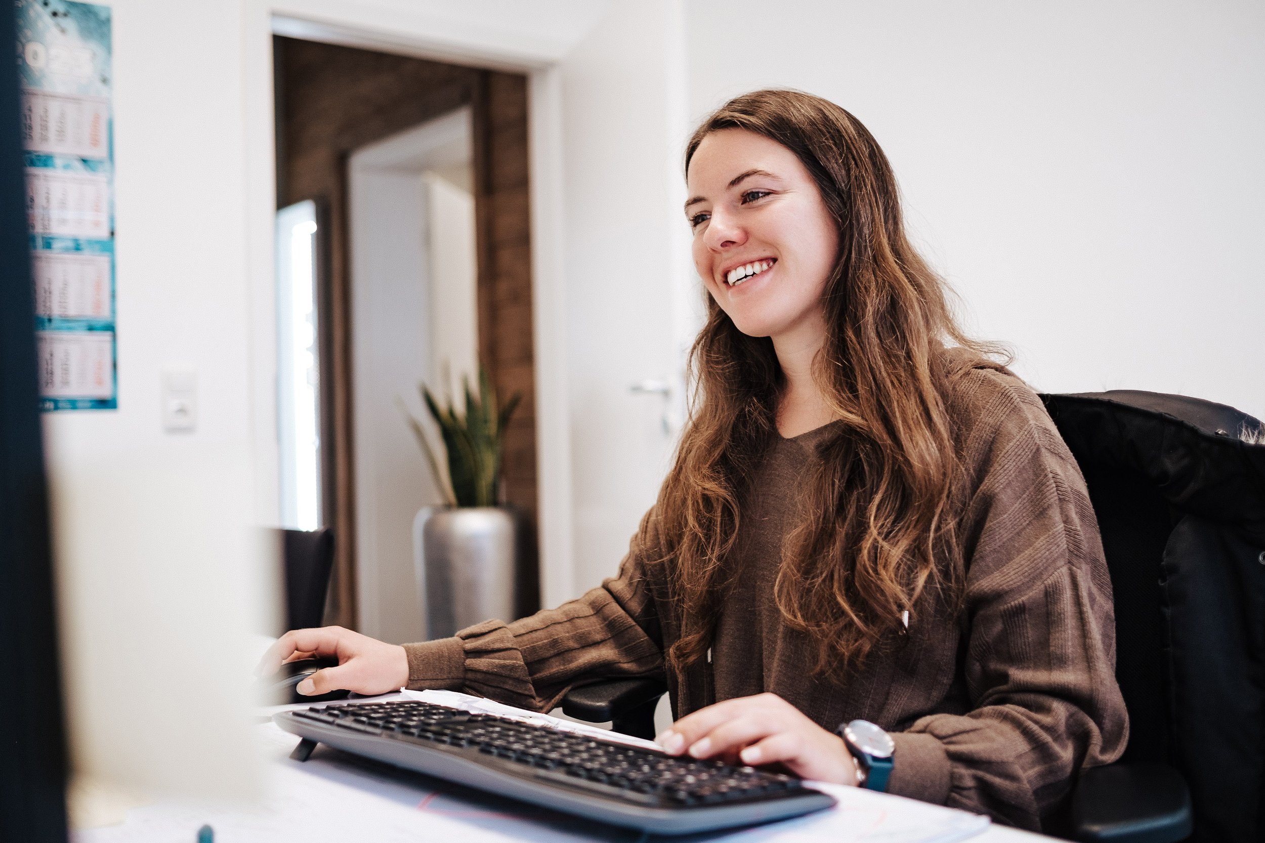Junge Frau arbeitet am Computer in einem Büro, lächelnd.