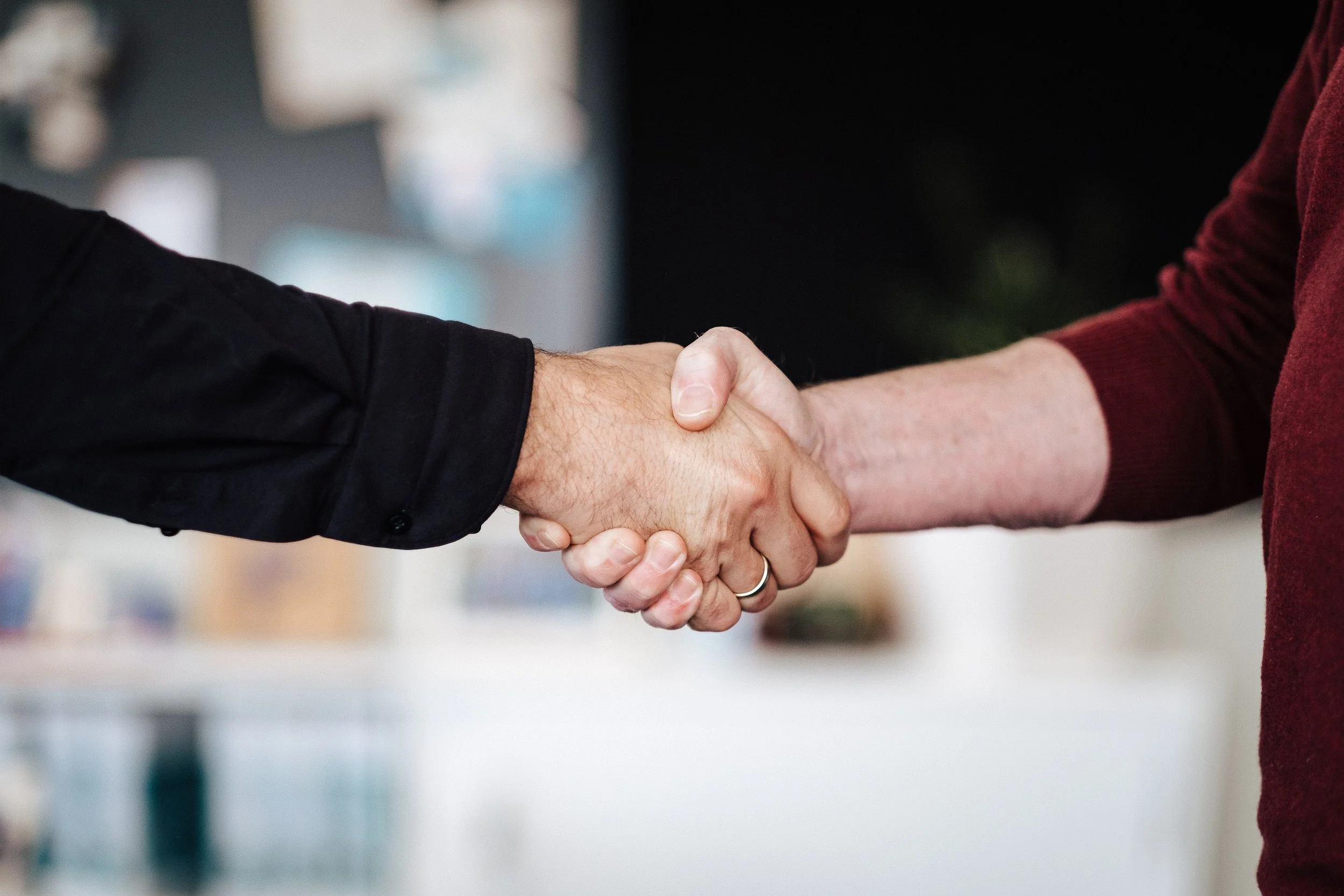 Zwei Menschen schütteln sich die Hände, einer trägt einen schwarzen Hemd, der andere einen roten Pullover.