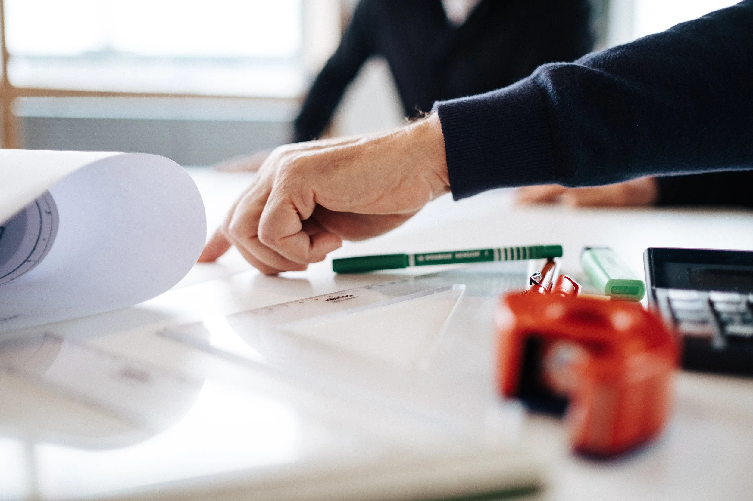 Eine Person arbeitet an einem Tisch mit Papier, einem Marker, einem Lineal, einem Taschenrechner und anderen Büroartikeln.