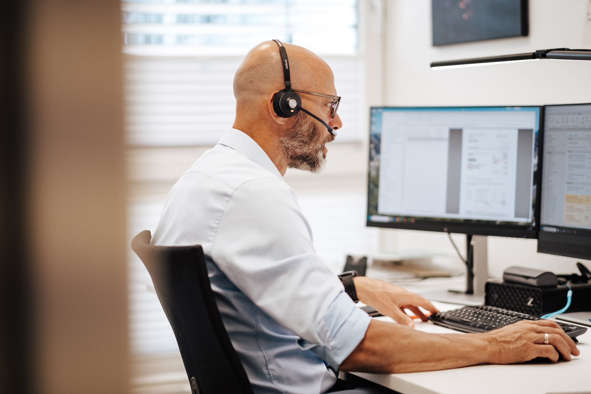 Mann mit Headset arbeitet an Computer mit zwei Monitoren im Büro.