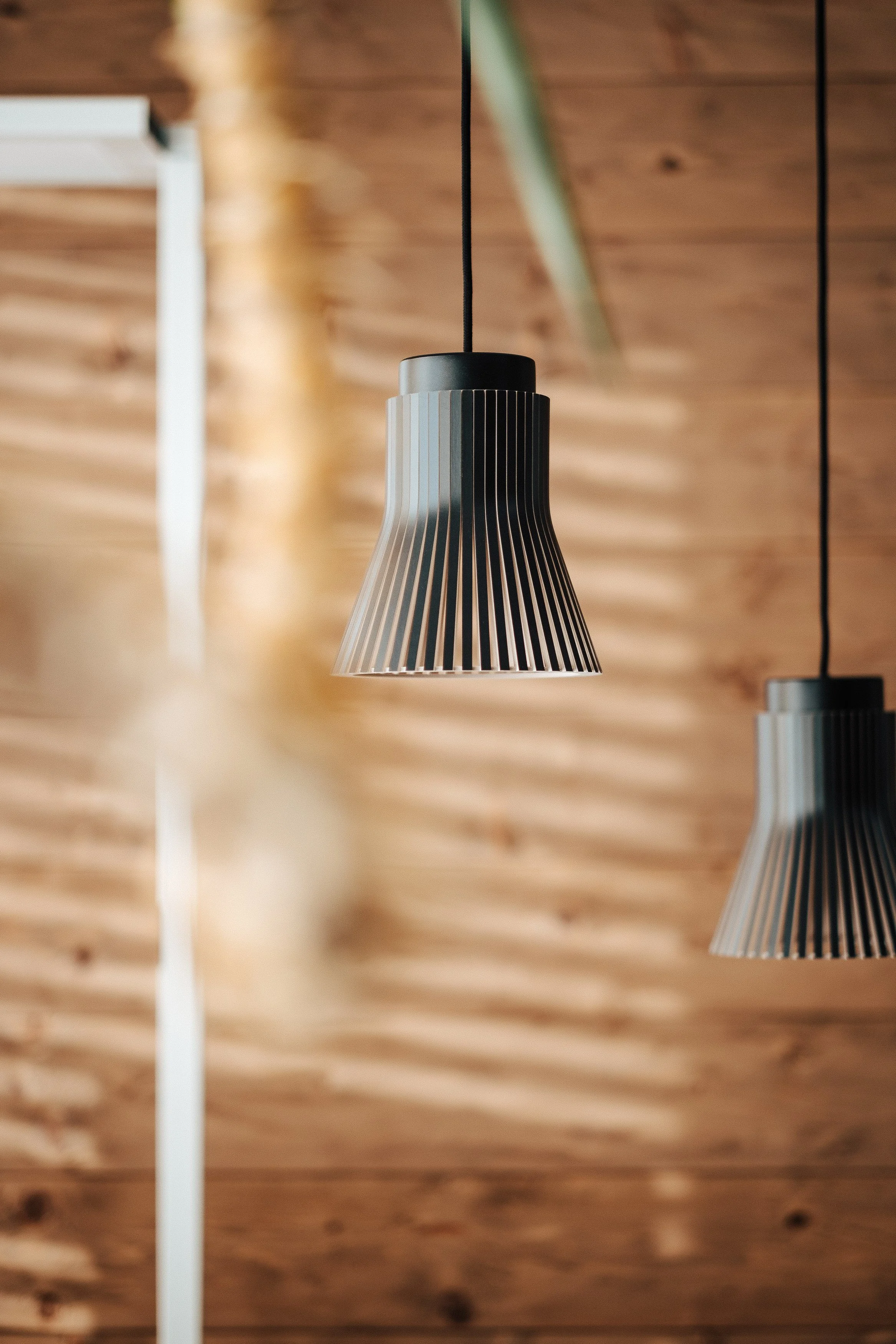 Drei moderne hängende Lampen mit schwarzen Schirmen und vertikalen Linien, vor einer Holzwand.