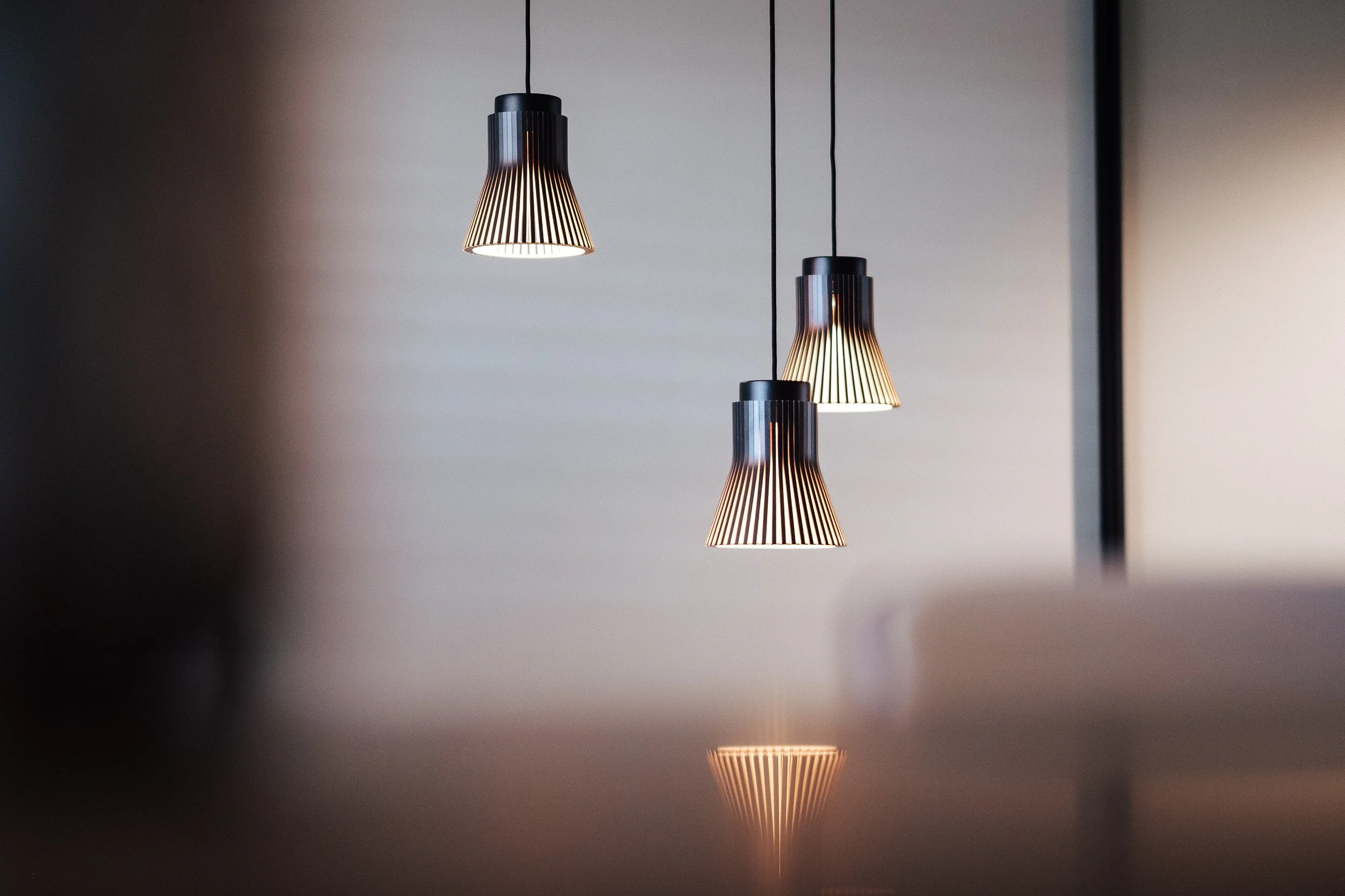 Drei moderne Hängeleuchten hängen an der Decke, Licht strahlt nach unten, reflektiert auf einer Tischfläche, dunkler Hintergrund.