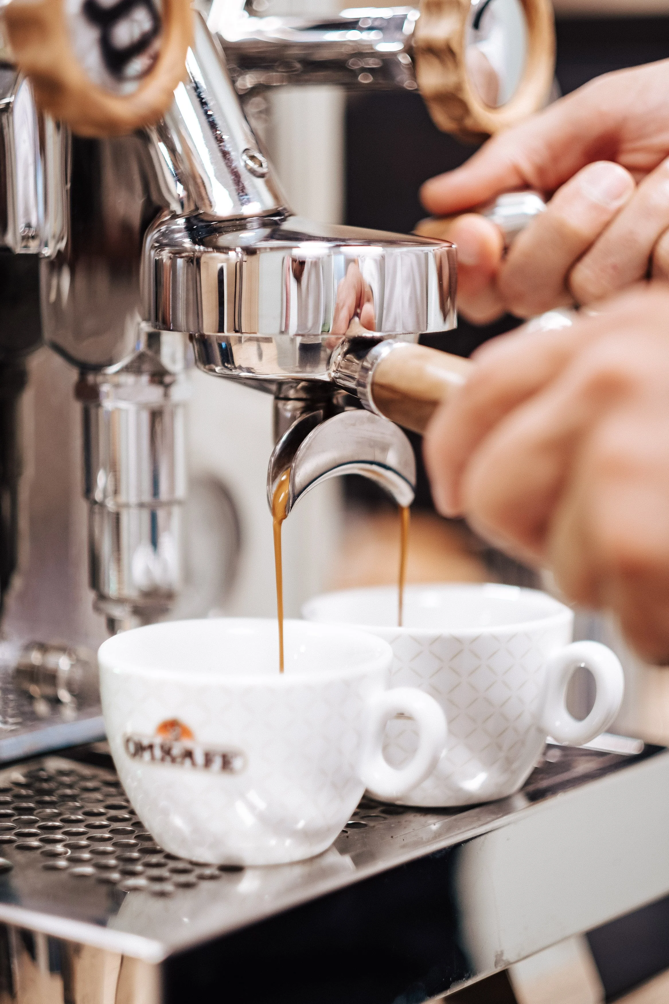 Der Espresso wird aus einer Espressomaschine in zwei weiße Tassen mit Mustern eingegossen.