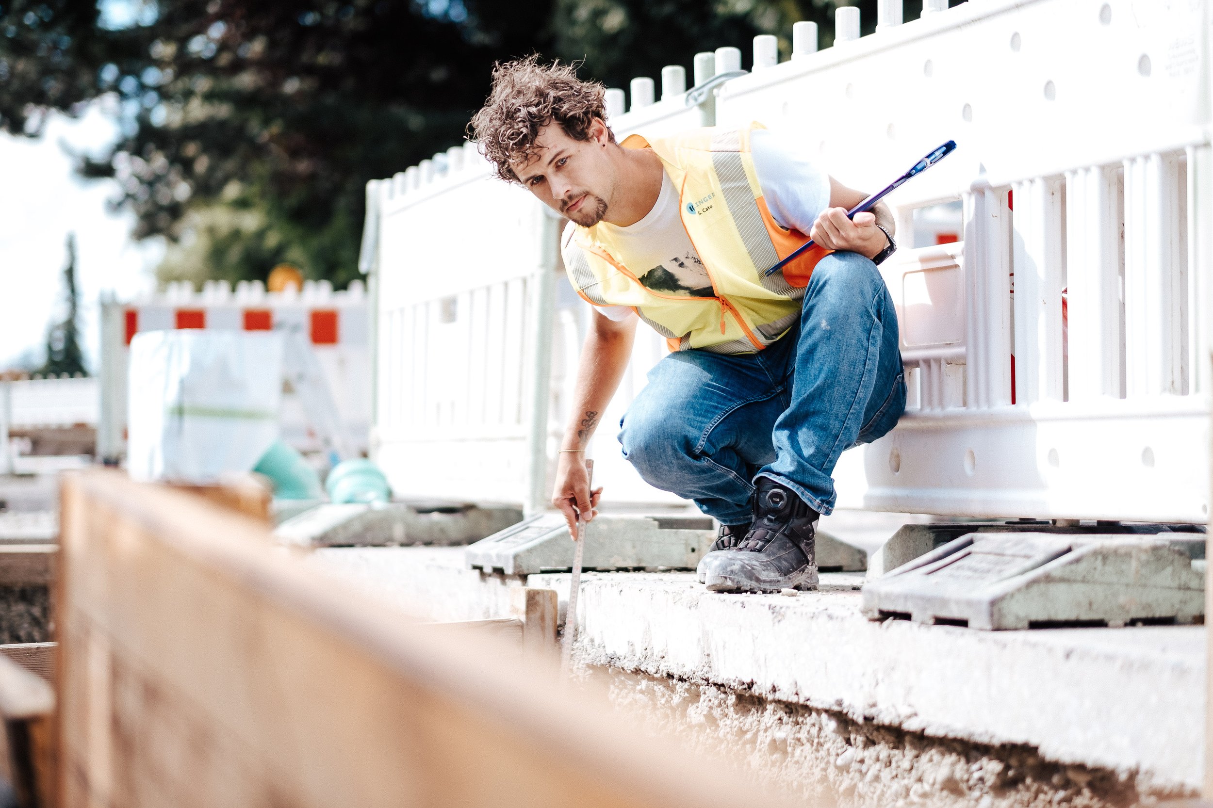 Ein Mann auf einer Baustelle, der Messungen vornimmt, trägt eine gelbe Sicherheitsweste und robustes Schuhwerk.