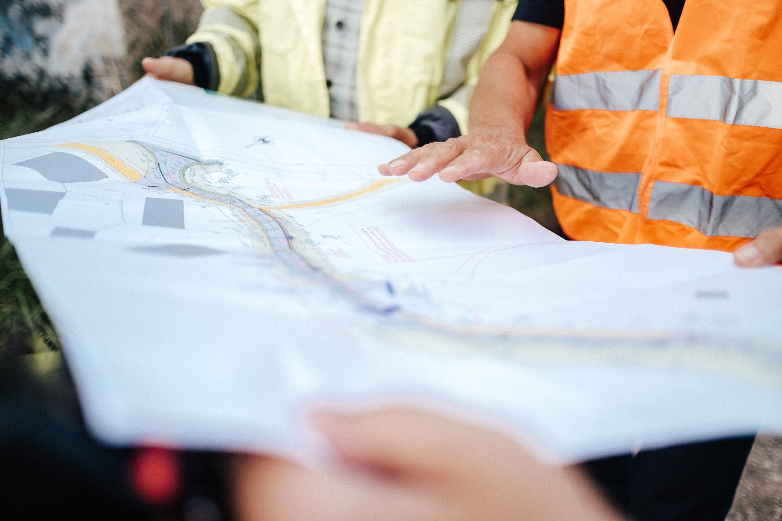 Zwei Personen betrachten eine große Karte im Freien, eine trägt eine orange Sicherheitsweste, die andere eine gelbe Jacke.
