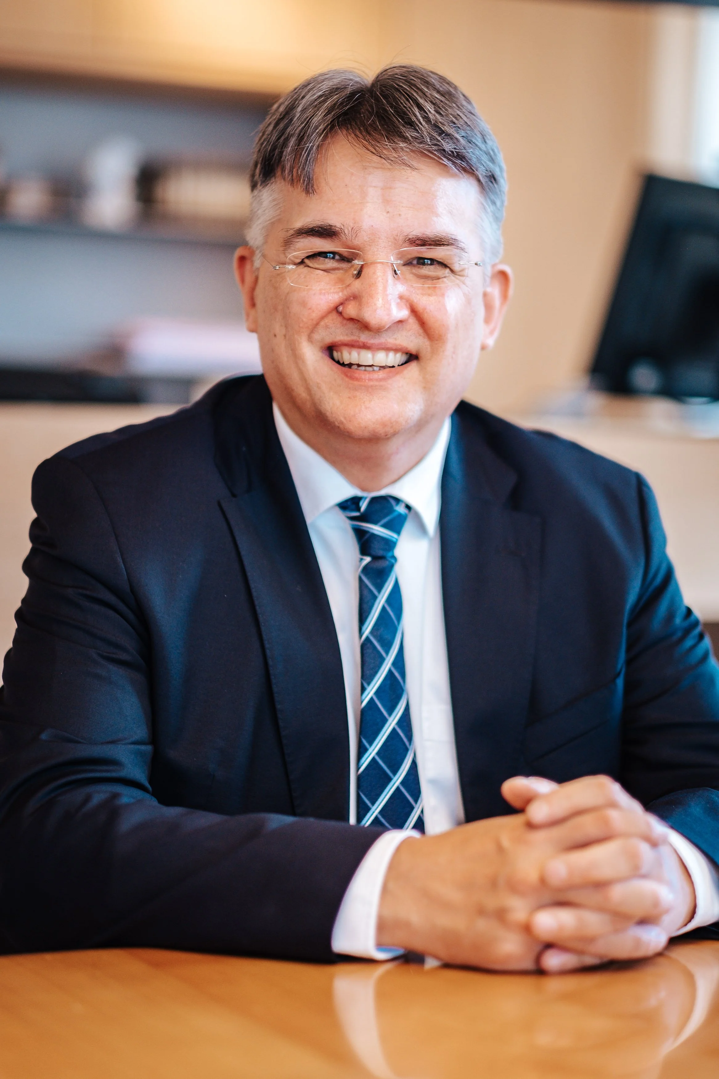 Ein lachender Mann in einem Anzug sitzt an einem Tisch in einem Büro.