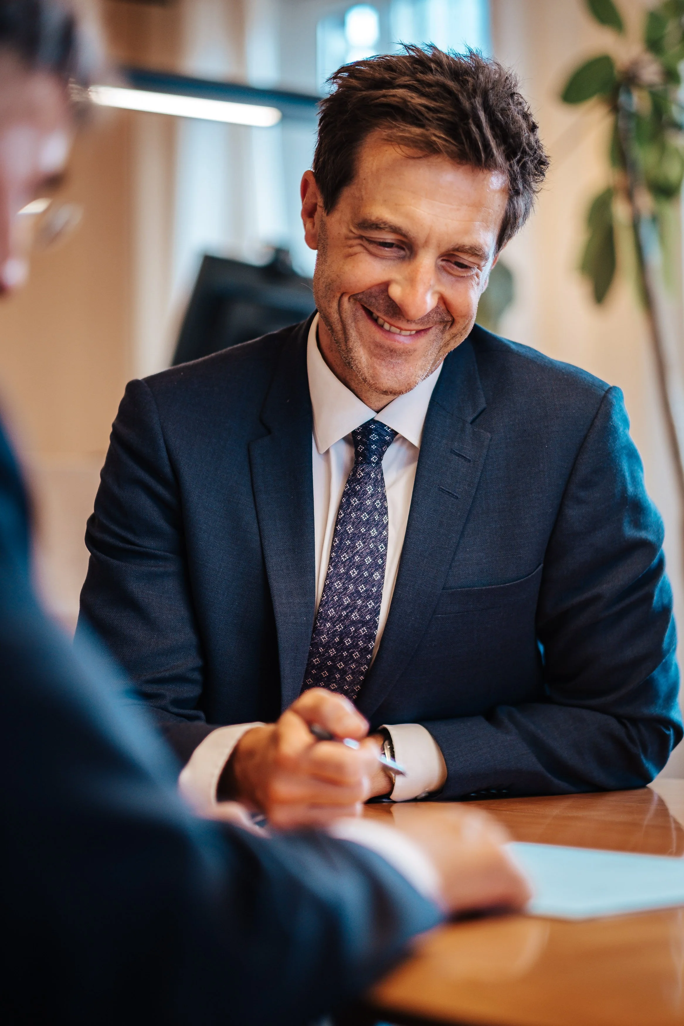 Ein Mann im Anzug lächelt während eines Gesprächs in einem Büro.