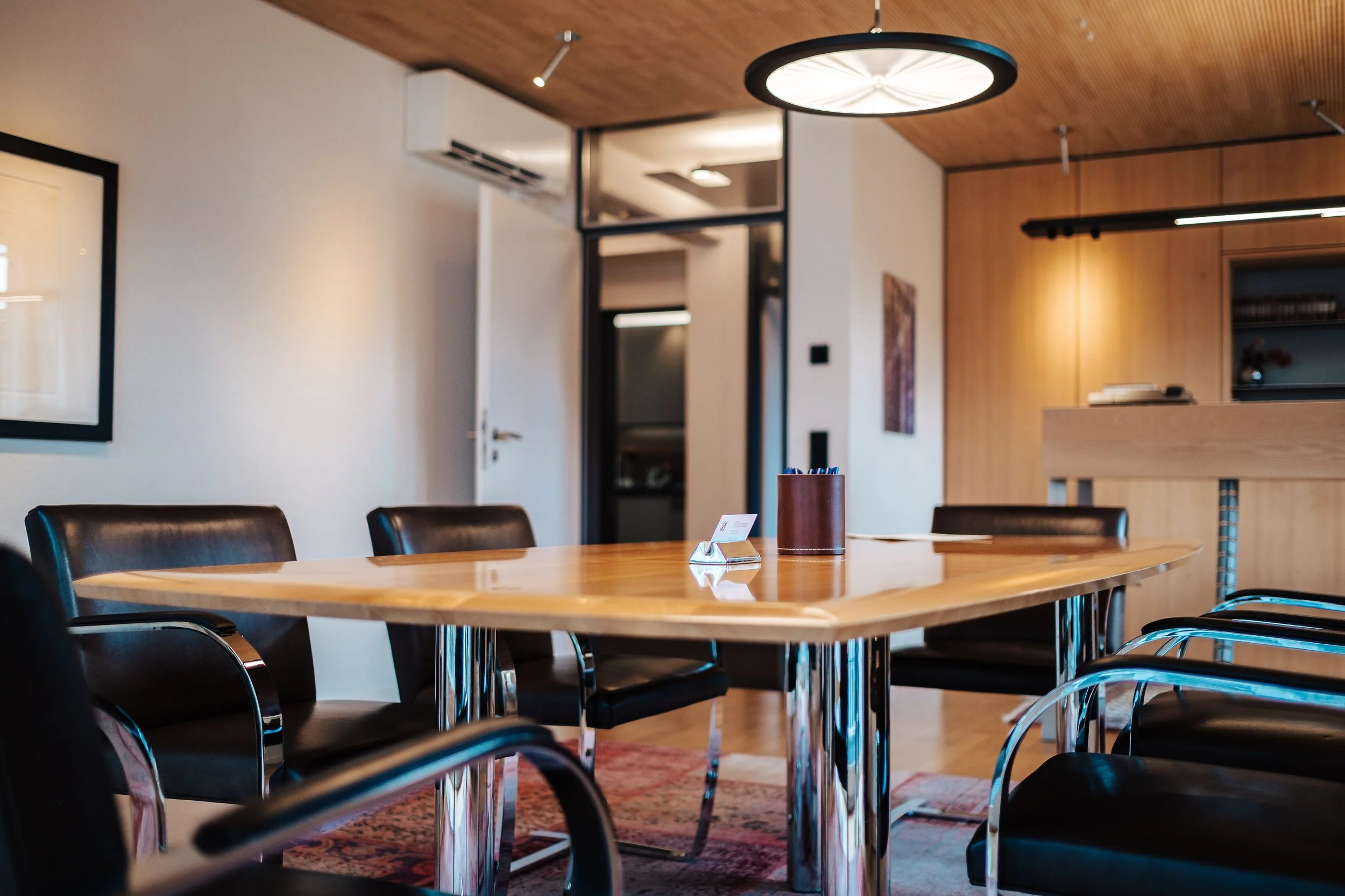 Ein Konferenztisch mit schwarzen Stühlen in einem modernen Büroraum, auf dem Tisch befindet sich ein Kasten mit Kugelschreibern und ein Namensschild.