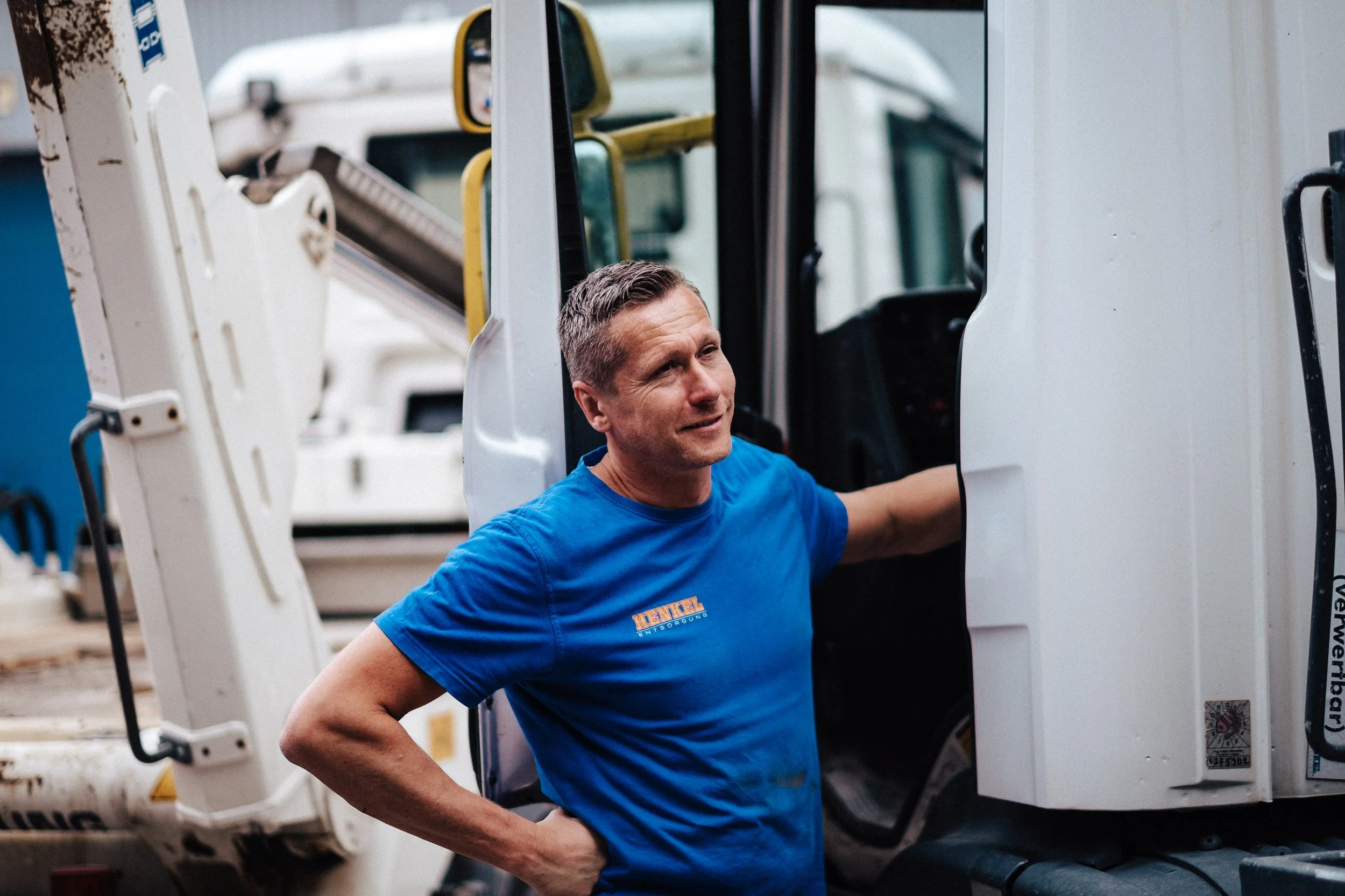 Mann in blauer Arbeitskleidung steht neben Baugerät, auf Baustelle.