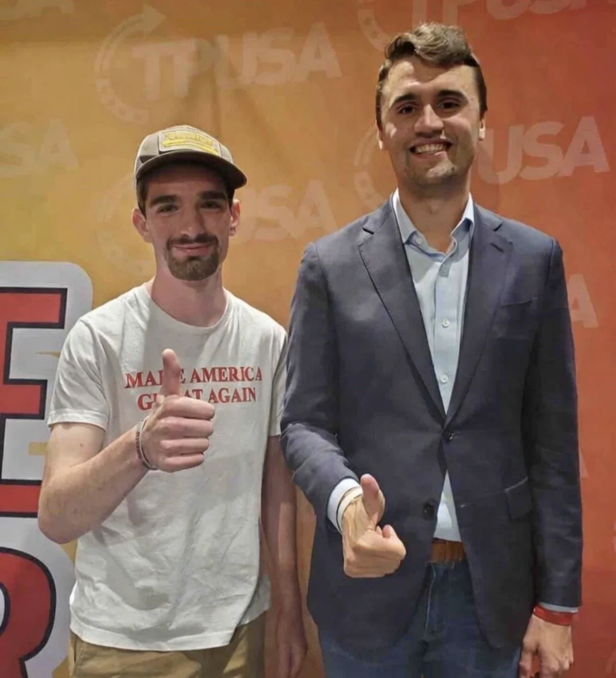 Two men standing side by side smiling and giving thumbs-up signs, with an orange background bearing the word 'USA' repeatedly. The man on the left is wearing a gray cap and a white t-shirt with red text that reads 'MAKE AMERICA GREAT AGAIN.' The man 