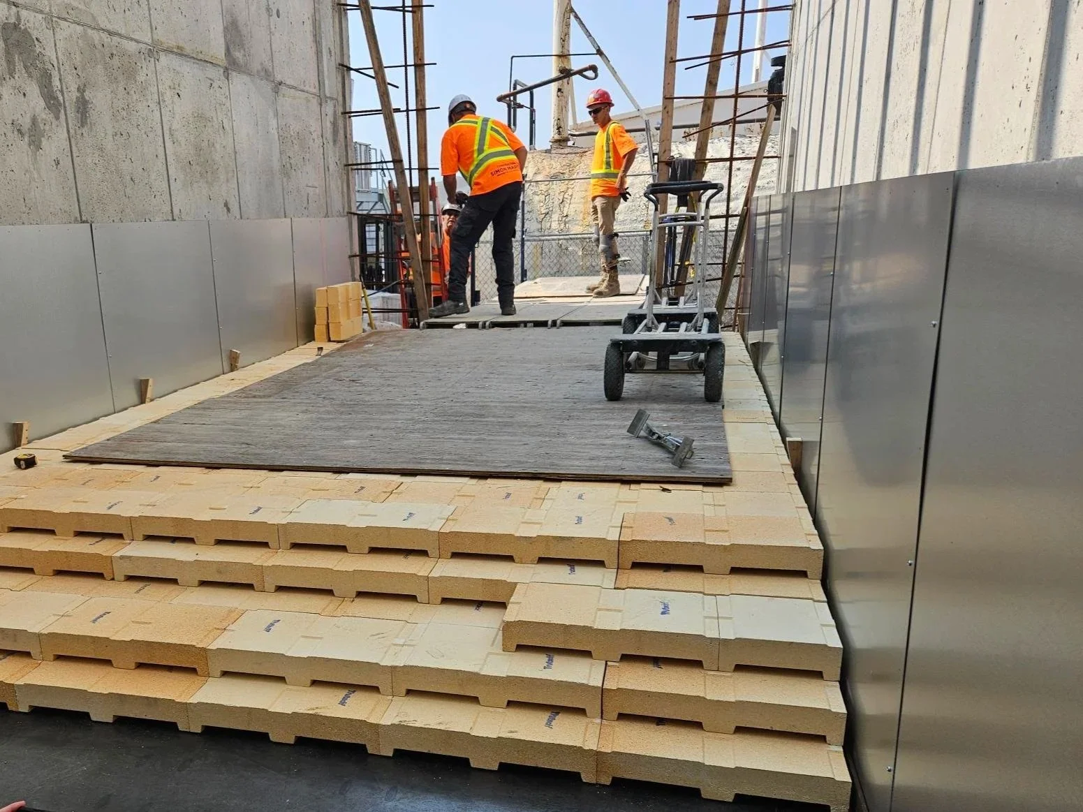 Travailleurs du bâtiment en pleine construction sur une plateforme, avec des matériaux isolants empilés en dessous.