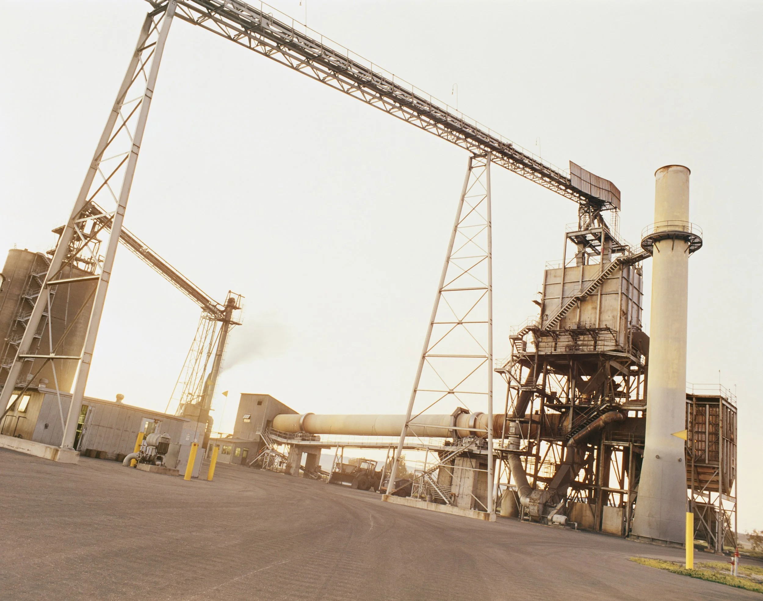 Une usine industrielle avec des installations métalliques, des pipelines et une cheminée, sous un ciel clair.