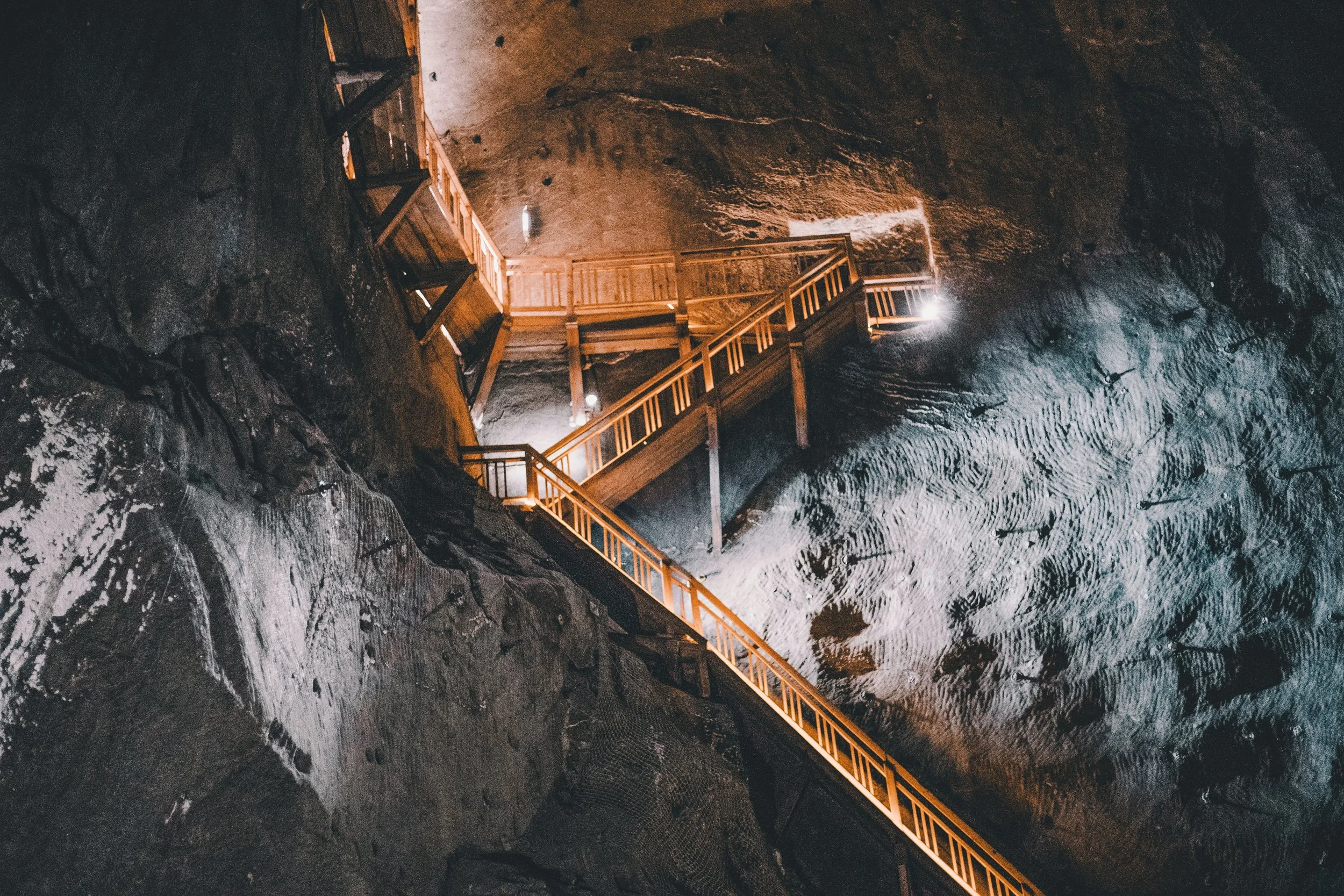 Passerelle en bois dans une grande grotte sombre, éclairée par des lumières suspendues.