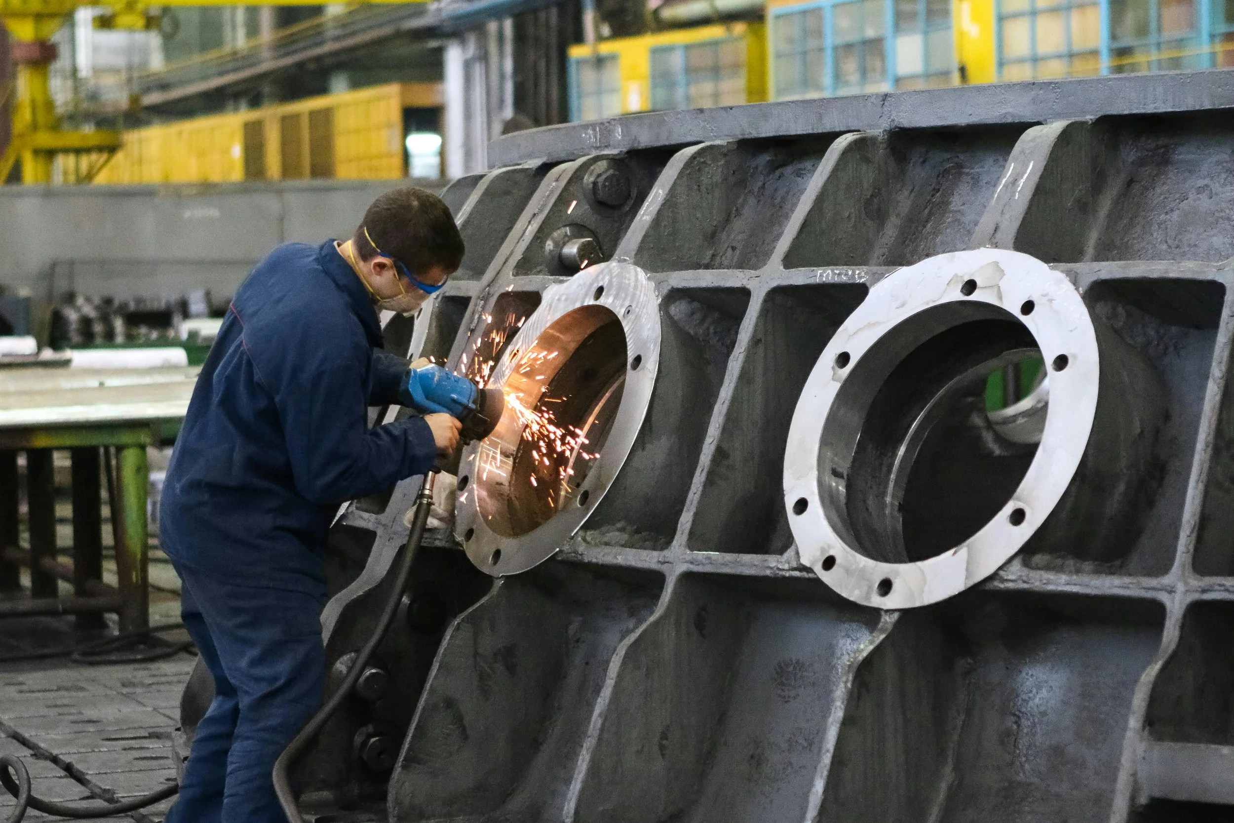 Worker welding a large industrial metal component in a factory setting.