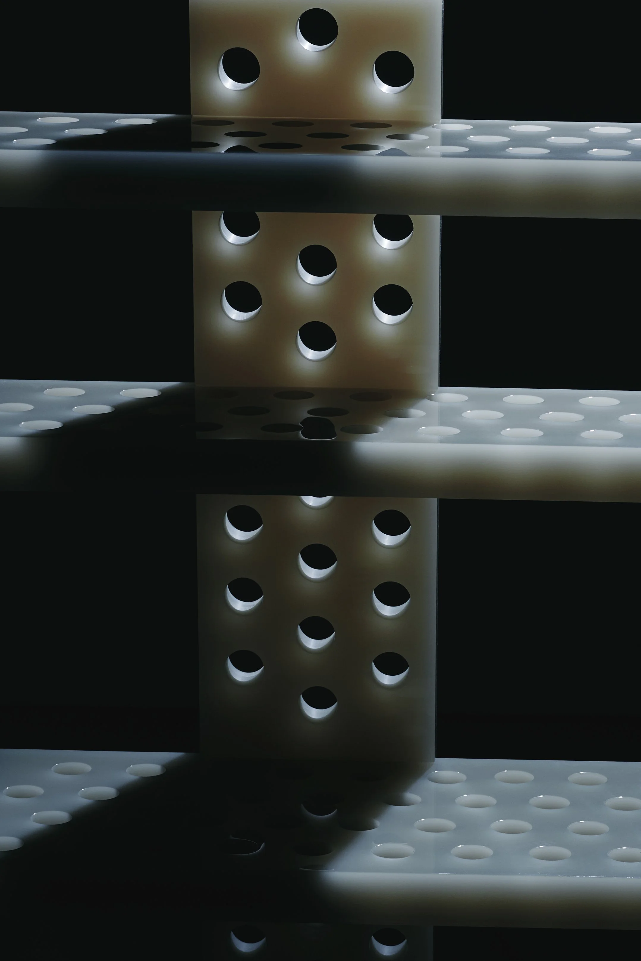 Close-up of a structure with multiple rows of circular holes, possibly part of an industrial or architectural element, illuminated in a dark setting.