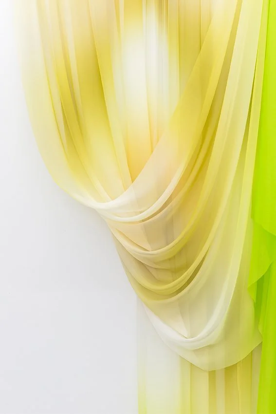 Softly draped yellow and green sheer fabric against a plain background.