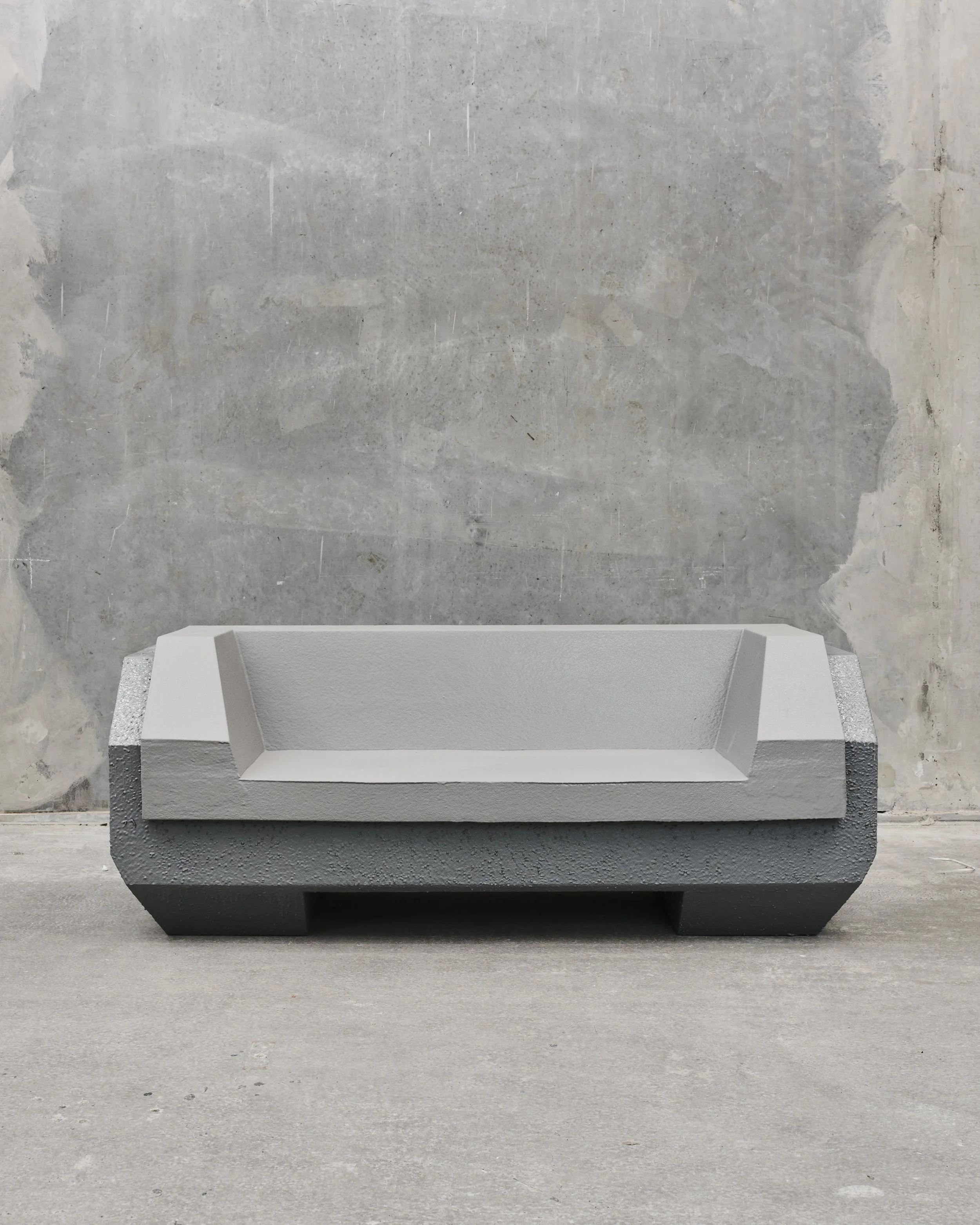 Minimalist gray concrete bench with angular design against a textured wall.